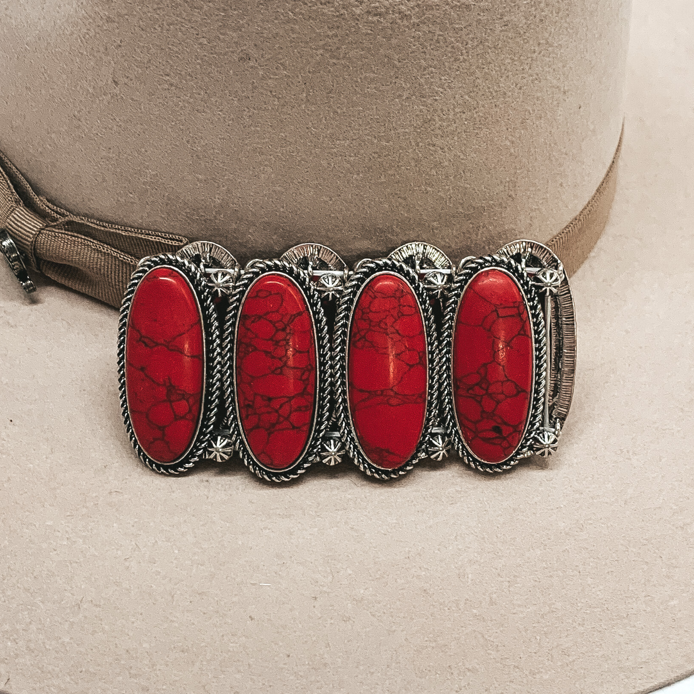 Silver bracelet with big oval red stones pictured laying on a beige background.