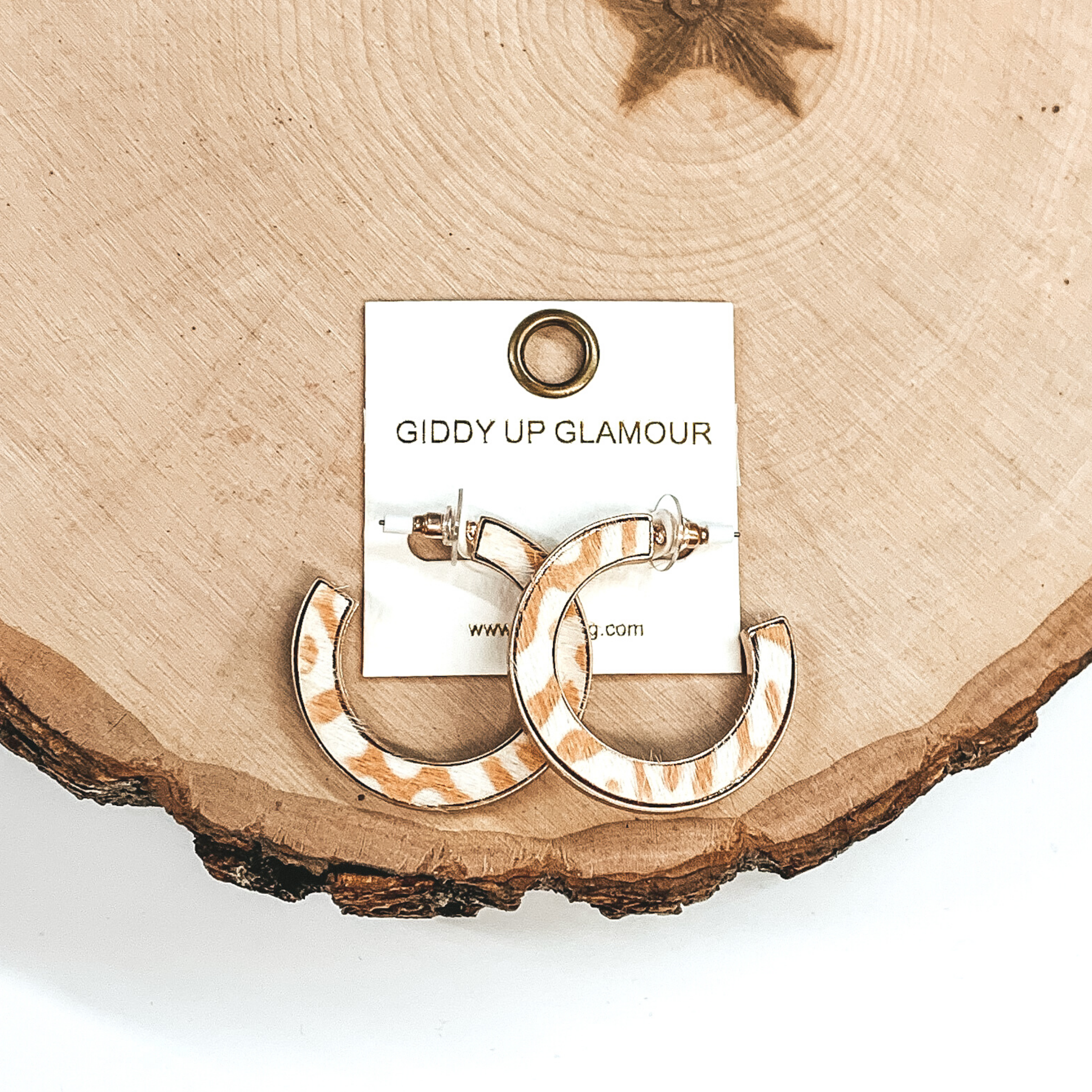 Gold hoops with white and tan animal print inlay. These earrings are pictured laying on a piece of wood on a white background.