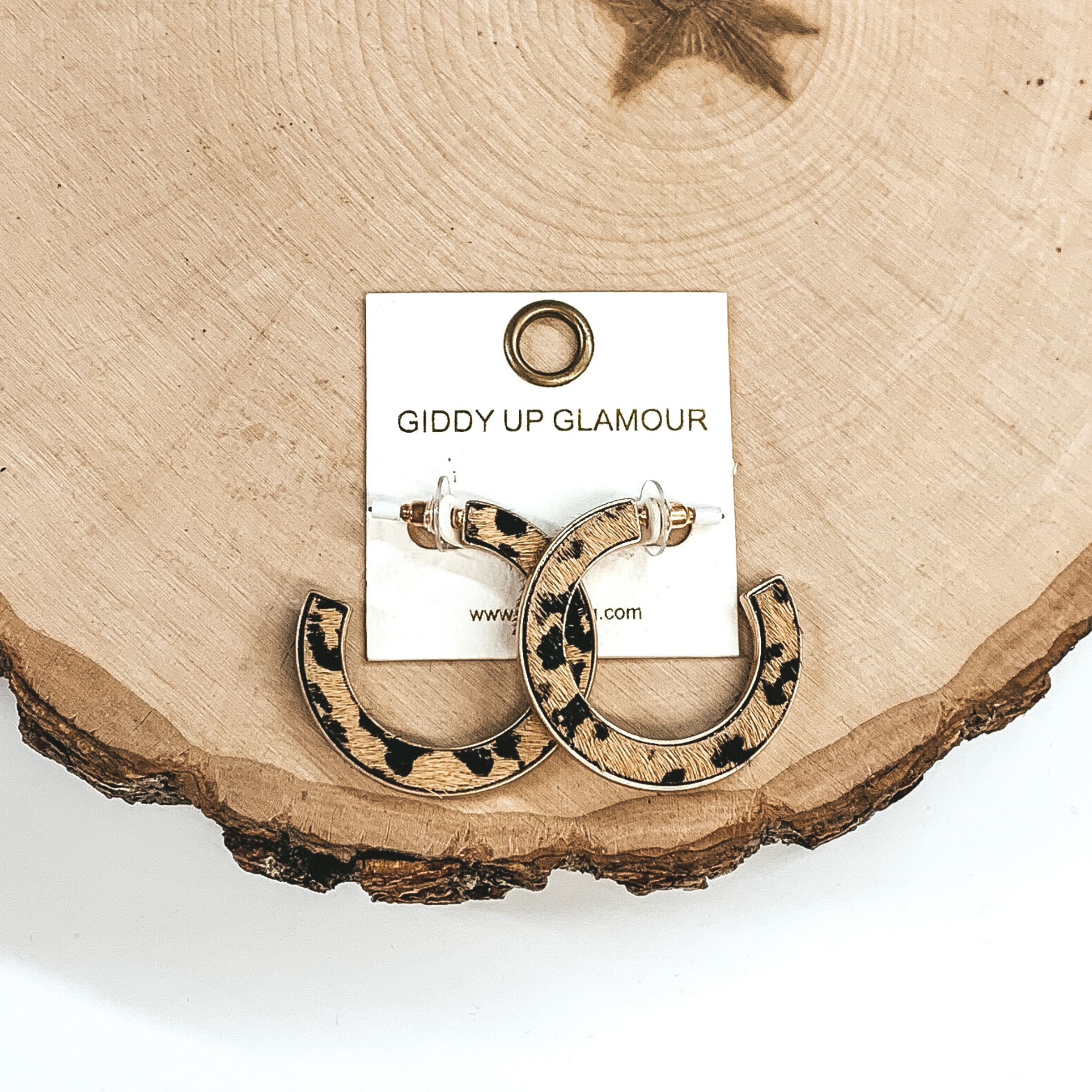 Gold hoops with brown and black animal print inlay. These earrings are pictured laying on a piece of wood on a white background.