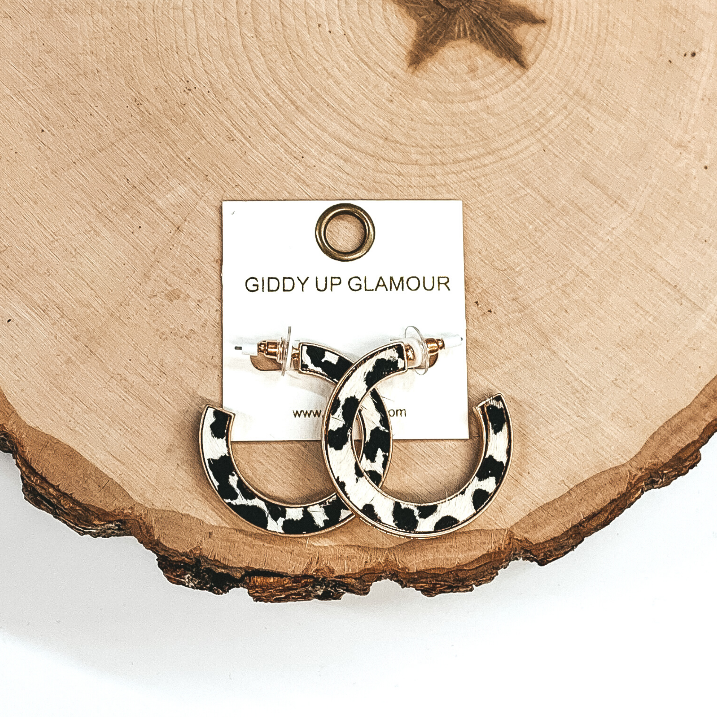 Gold hoops with white and black animal print inlay. These earrings are pictured laying on a piece of wood on a white background.