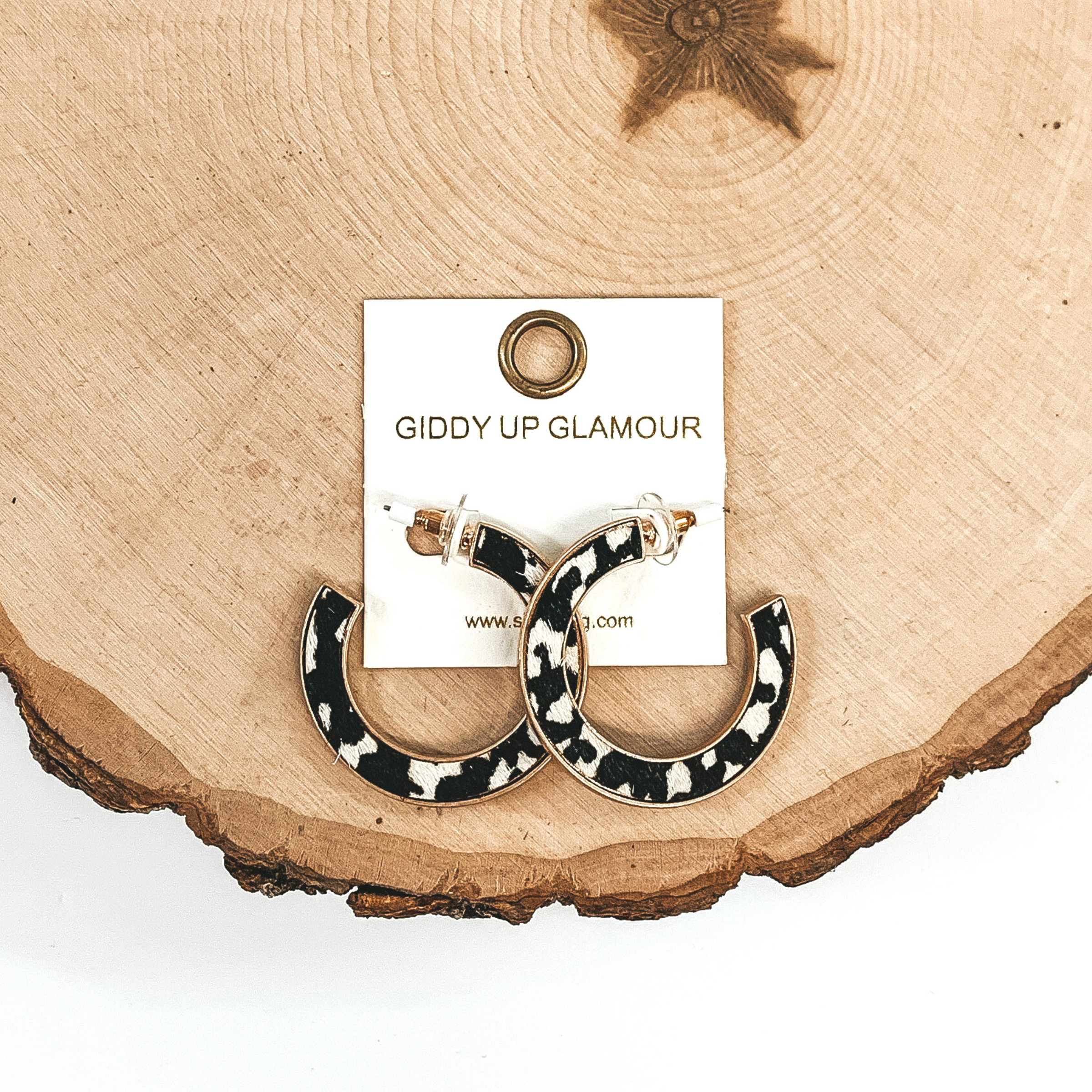 Gold hoops with black and white animal print inlay. These earrings are pictured laying on a piece of wood on a white background.