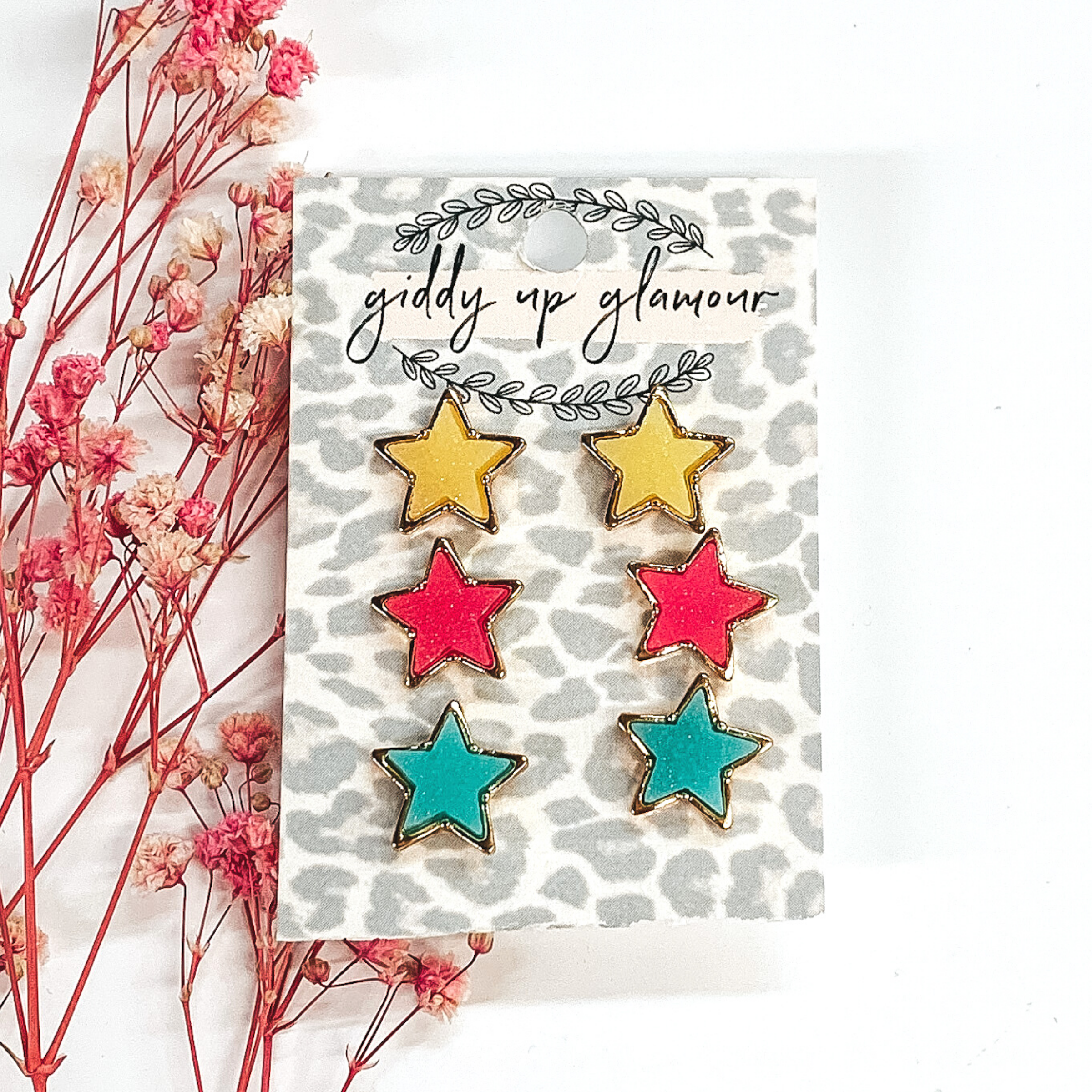 This earring set has gold star studs with a druzy inlay. It comes in the colors yellow, pink, and teal. This earring set is pictured on a white background and pink baby breaths. 