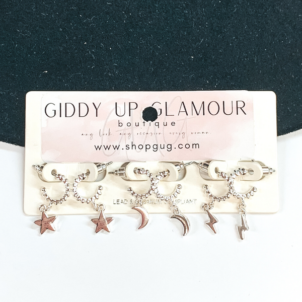 This silver earrings set has tiny twisted hoops with dangle charms. There are star charms, moon charms, and lightning bolt charms. These earrings are pictured on a earring cardstock that is on a white and black background.