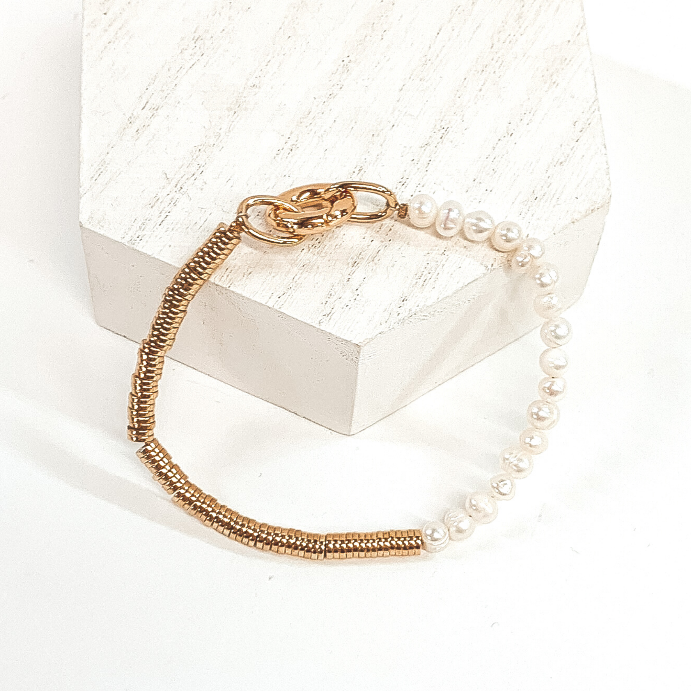 This bracelet is half gold disk metal beads and half white pearl beads. This bracelet has a gold closure to have an easy time to put on and off. This bracelet is pictured laying on white fixture on a white background. 