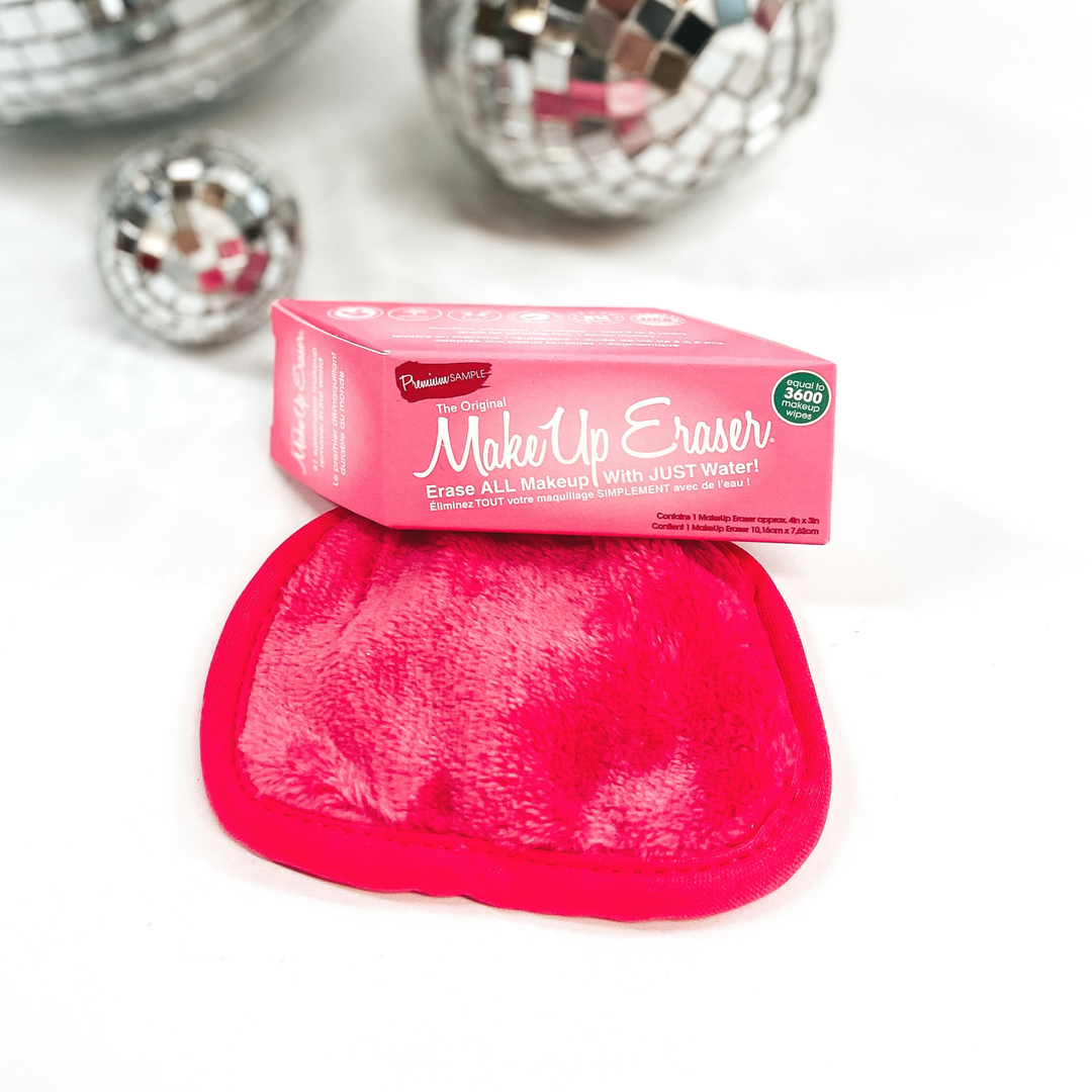 Hot pink rounded rectangle cloth with a pink box laying on a little bit of the cloth. The pink box says "Make Up Eraser" in big letters. This is all pictured on a white background with some disco balls in the top of the picture.  