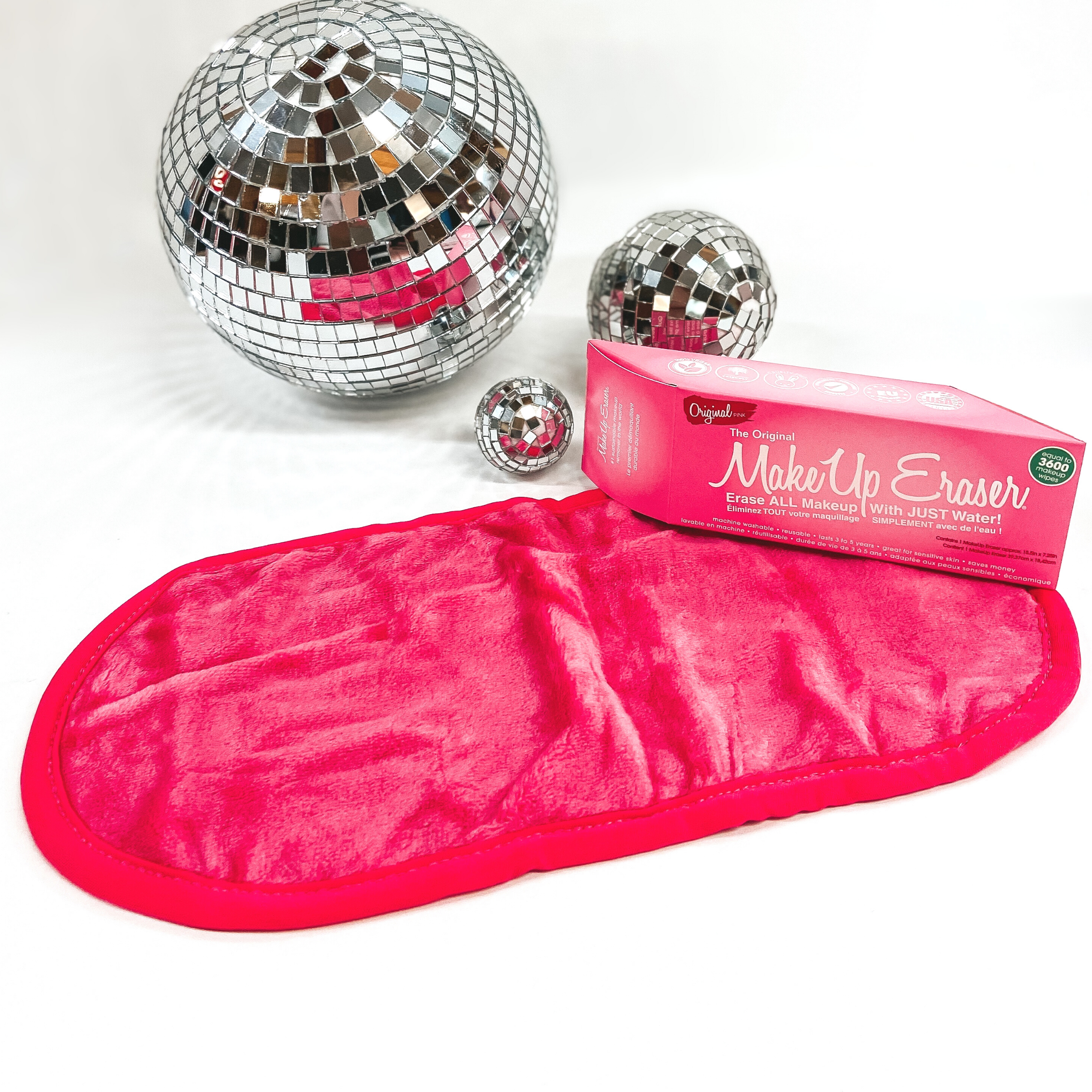 A hot pink long, rounded rectangle cloth is pictured with a pink box laying on one of the corners. This is pictured on a white background with a few disco balls in the top of the picture. 