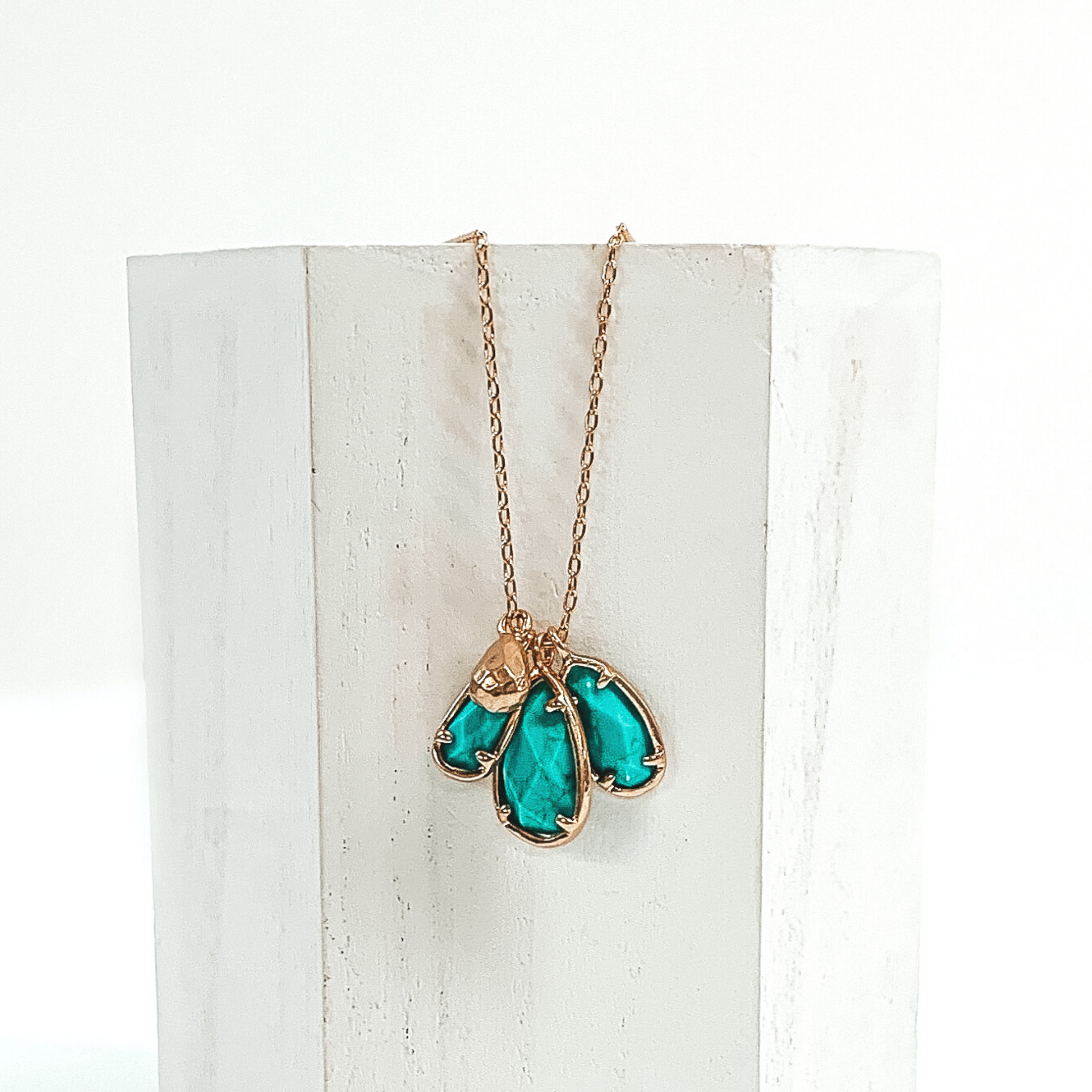 Small gold chain with three turquoise marbled teardrop stone pendants outlined in gold. It also has a tiny gold teardrop pendant. This necklace is pictured laying a white piece of wood on a white background.