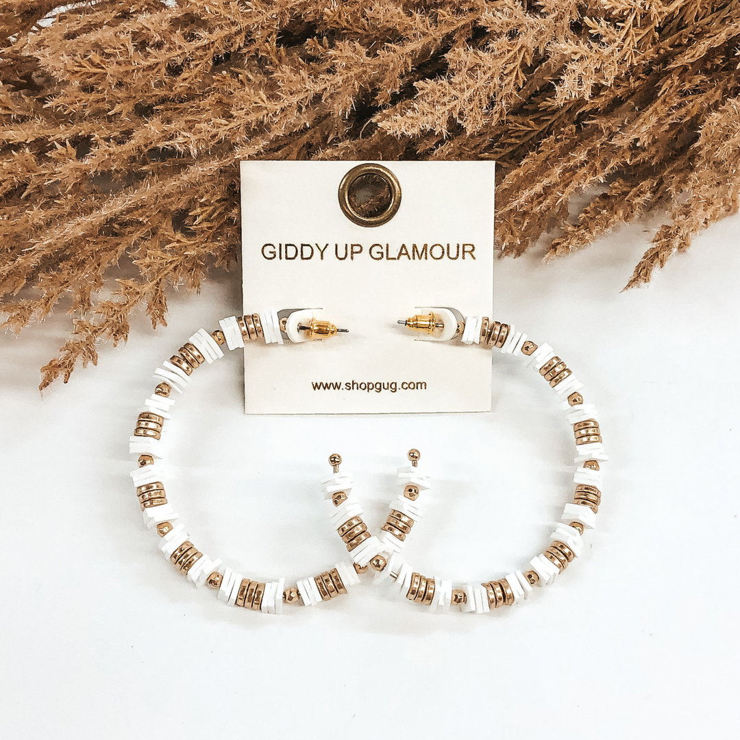 Beaded hoop earrings with square, white disk beads and gold beads. These earrings are pictured on a white background with brown floral at the top.