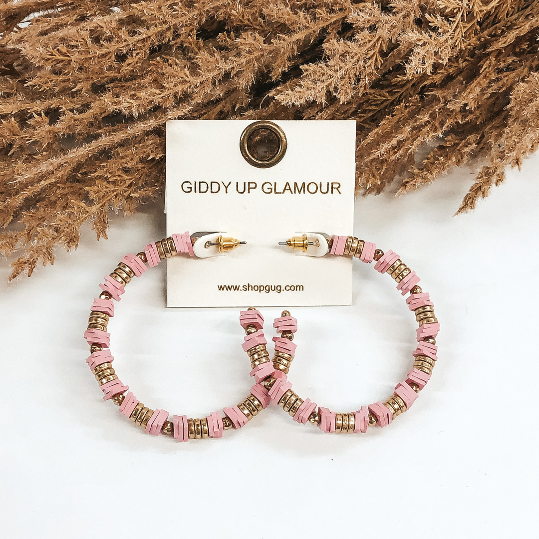 Beaded hoop earrings with square, light pink disk beads and gold beads. These earrings are pictured on a white background with brown floral at the top.