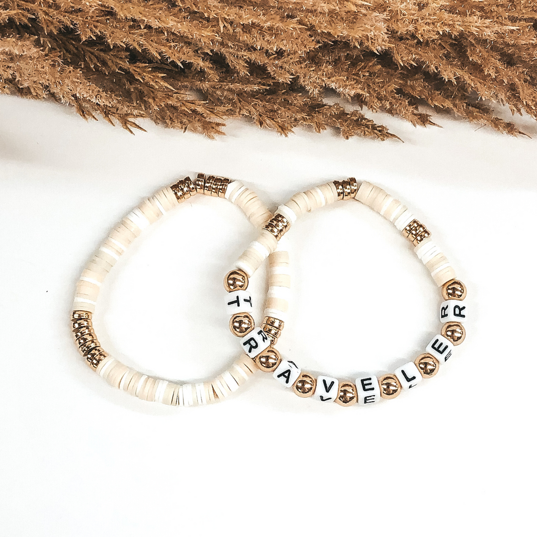 Two bracelets that has a mix of ivory colors and white disk beads. On one bracelet, you have three sections of gold disc beads. On the other bracelet you have three smaller section of gold disc beads and then letter beads that spell out "TRAVELER" with gold spacers in between. These bracelets are pictured on a white background.