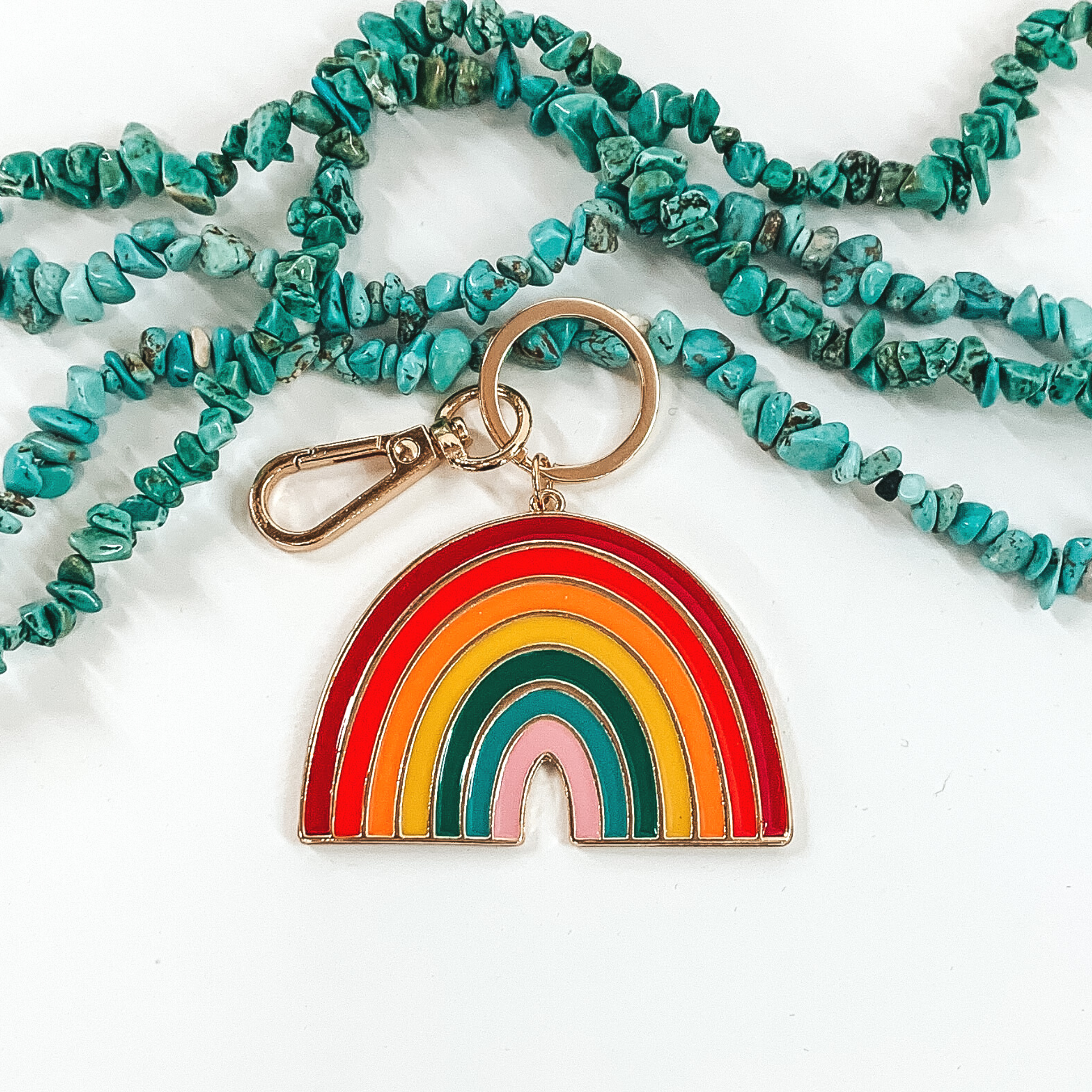 This is a gold chain with a rainbow pendant that includes the colors maroon, red, orange, yellow, green, light blue, and lilac. It is pictured on a white background with turquoise beads in at the top of the picture.