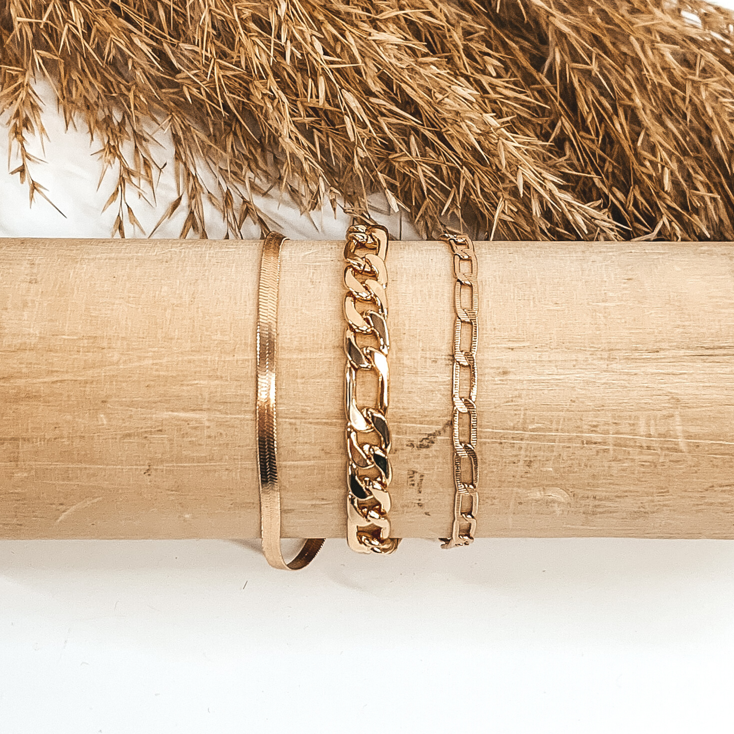 This gold bracelet includes four different types of chains. This bracelet is on a light colored piece of wood pictured on a white background with some tan floral at the top of the picture.