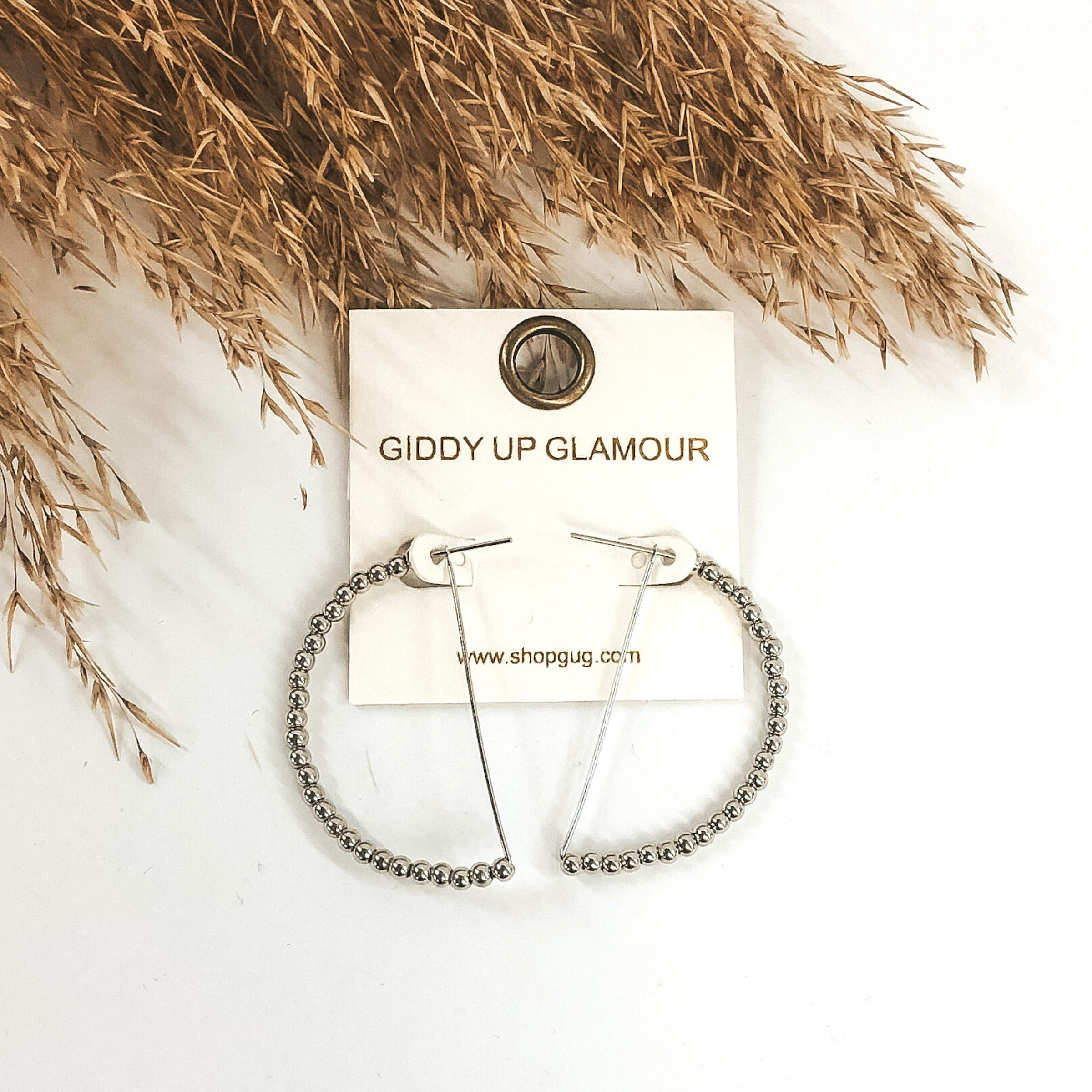 Silver semi circle hoop earrings with the curved part covered in silver beads. These earrings are pictured on a white background with tan floral at the top of the picture.