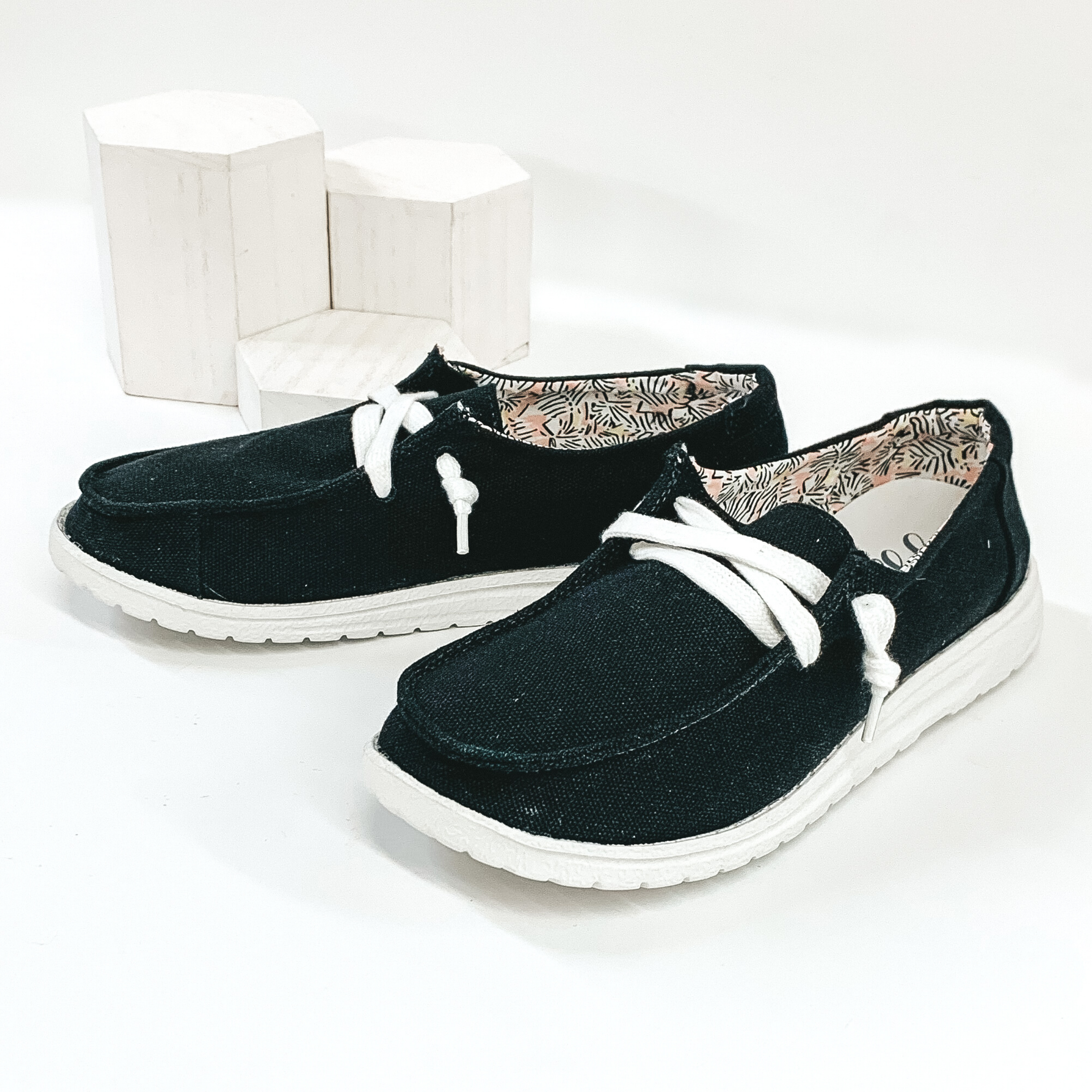 Black slip on canvas loafers with a white colored shoe lace and white sole. Pictured on white background.