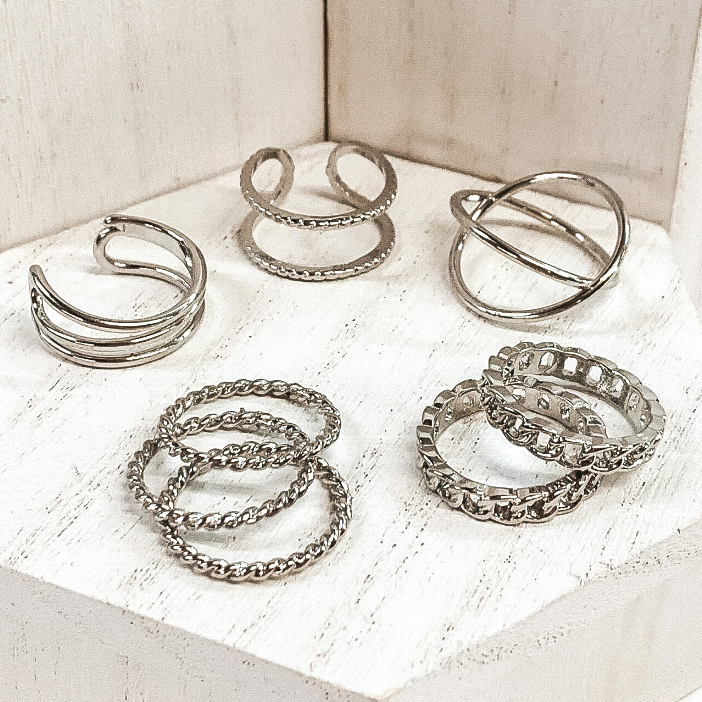 This is a eight piece silver ring set. Three rings are double in unique ways, there are three thin twisted rings, and the last two are chained rings. These rings are pictured on a white background. 