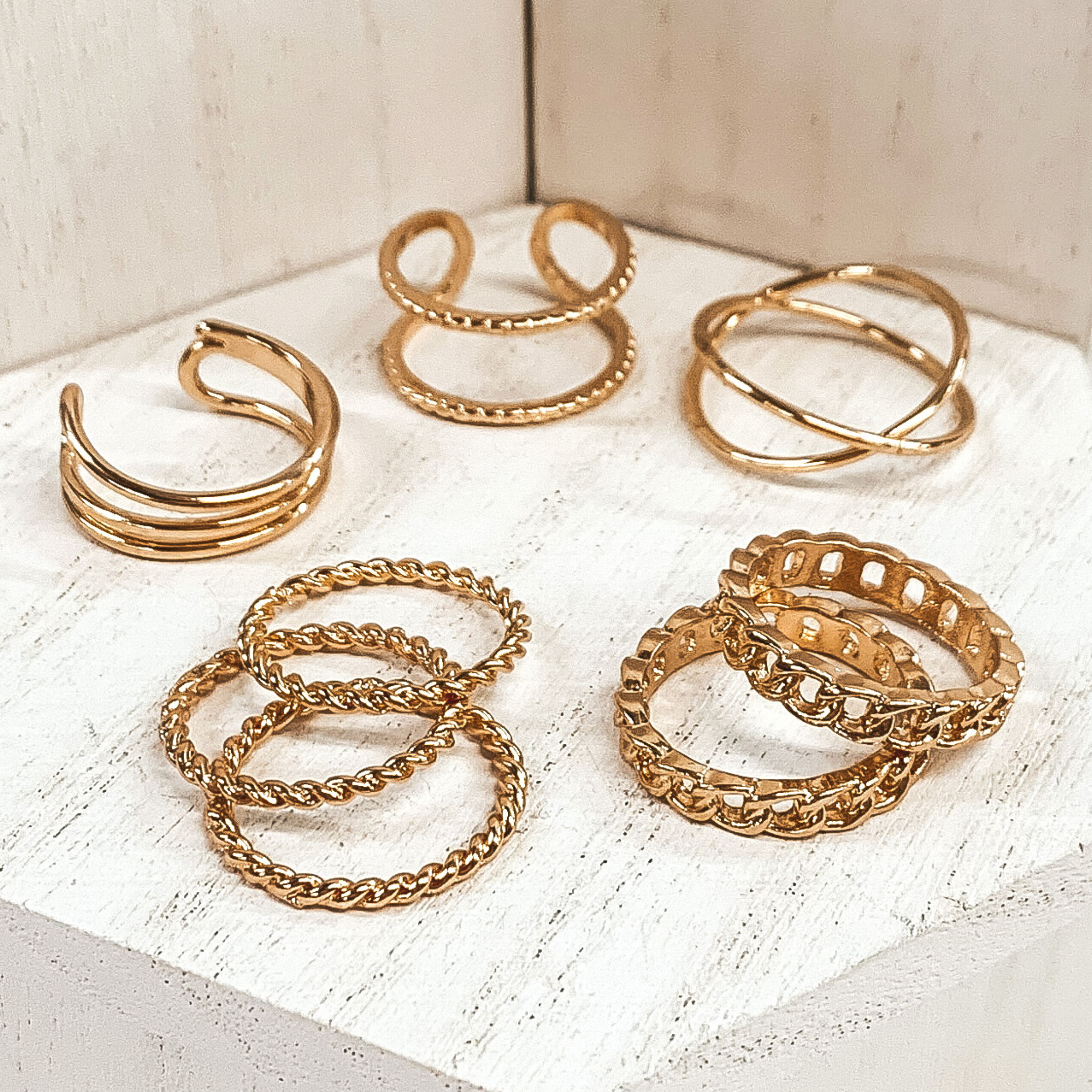 This is a eight piece gold ring set. Three rings are double in unique ways, there are three thin twisted rings, and the last two are chained rings. These rings are pictured on a white background.