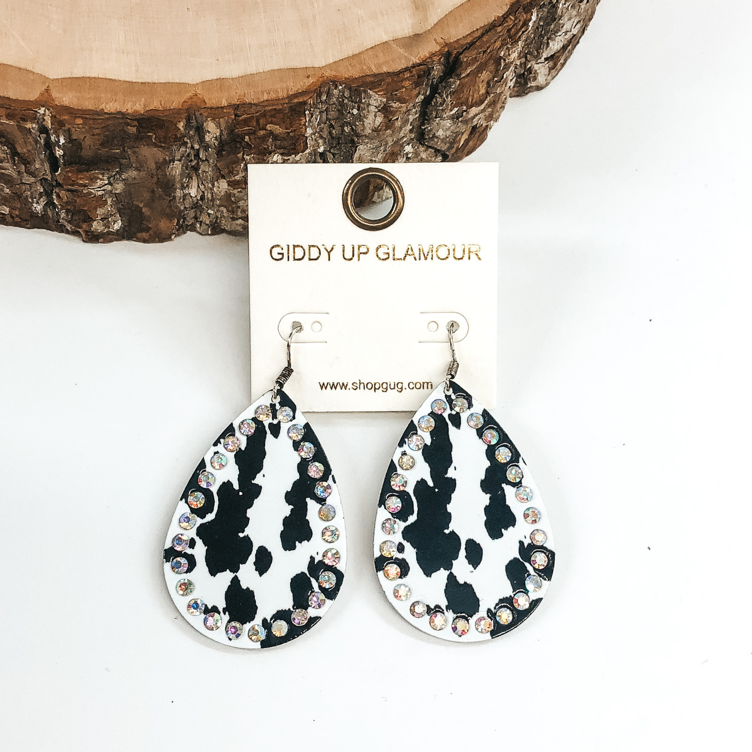 These are teardrop dangle earrings. These earrings have a black cow hide print with an AB crystal outline. These earrings are pictured on a white background with wood at the top of the picture.