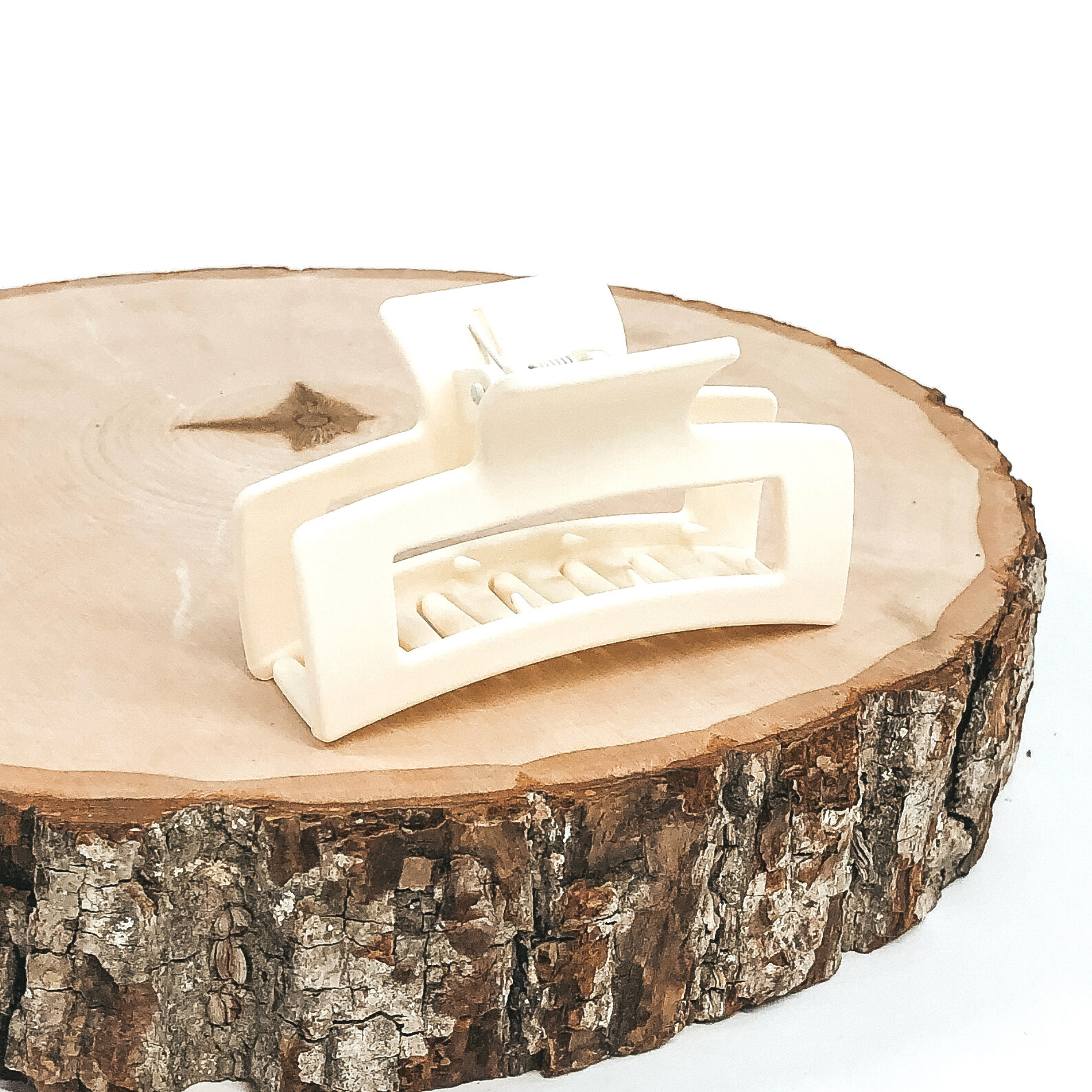 Matte ivory rectangle claw clip with rectangle cutout. This clip is pictured on a piece of wood on a white background. 
