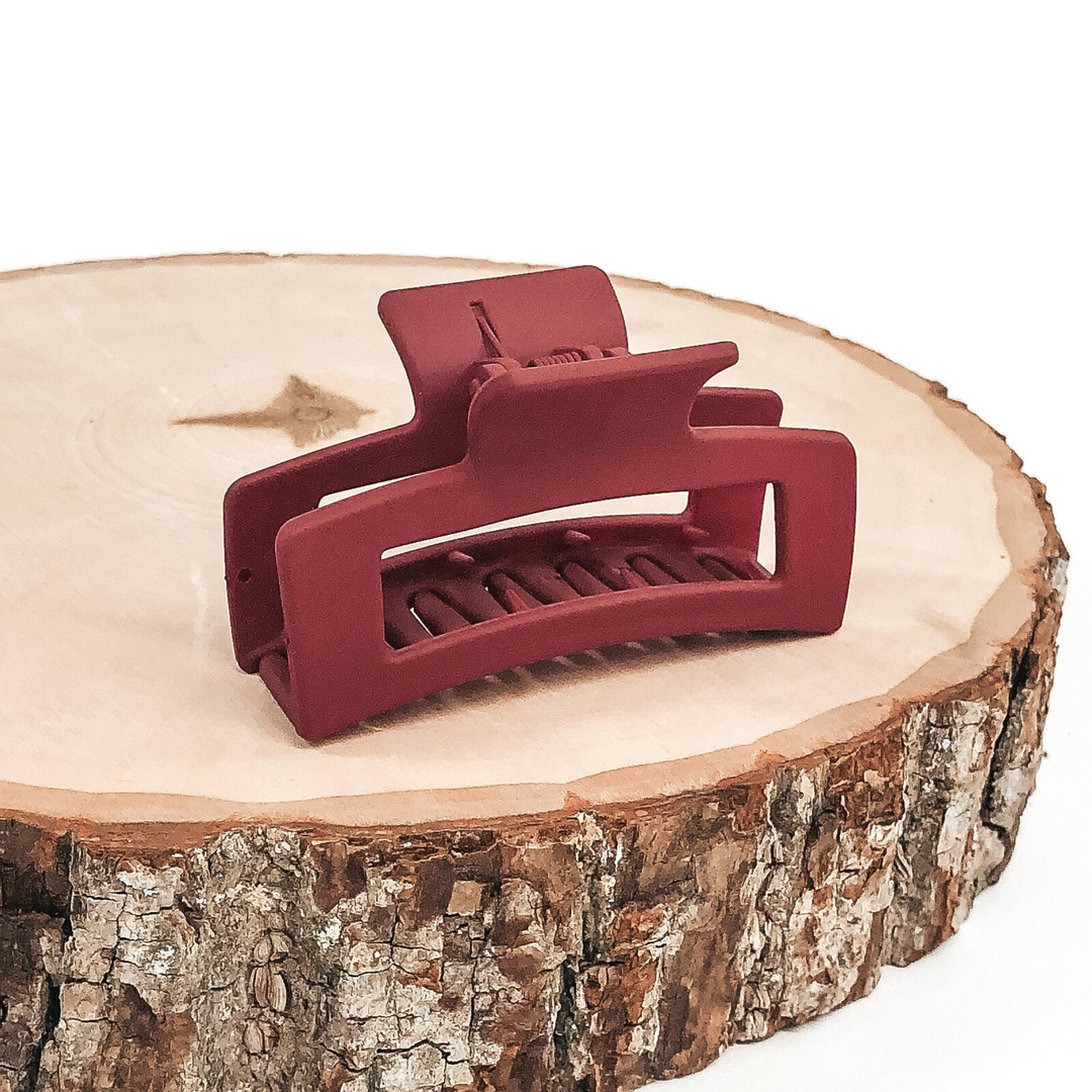 Matte red rectangle claw clip with rectangle cutout. This clip is pictured on a piece of wood on a white background.