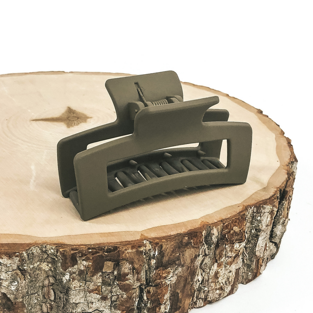Matte olive green rectangle claw clip with rectangle cutout. This clip is pictured on a piece of wood on a white background.