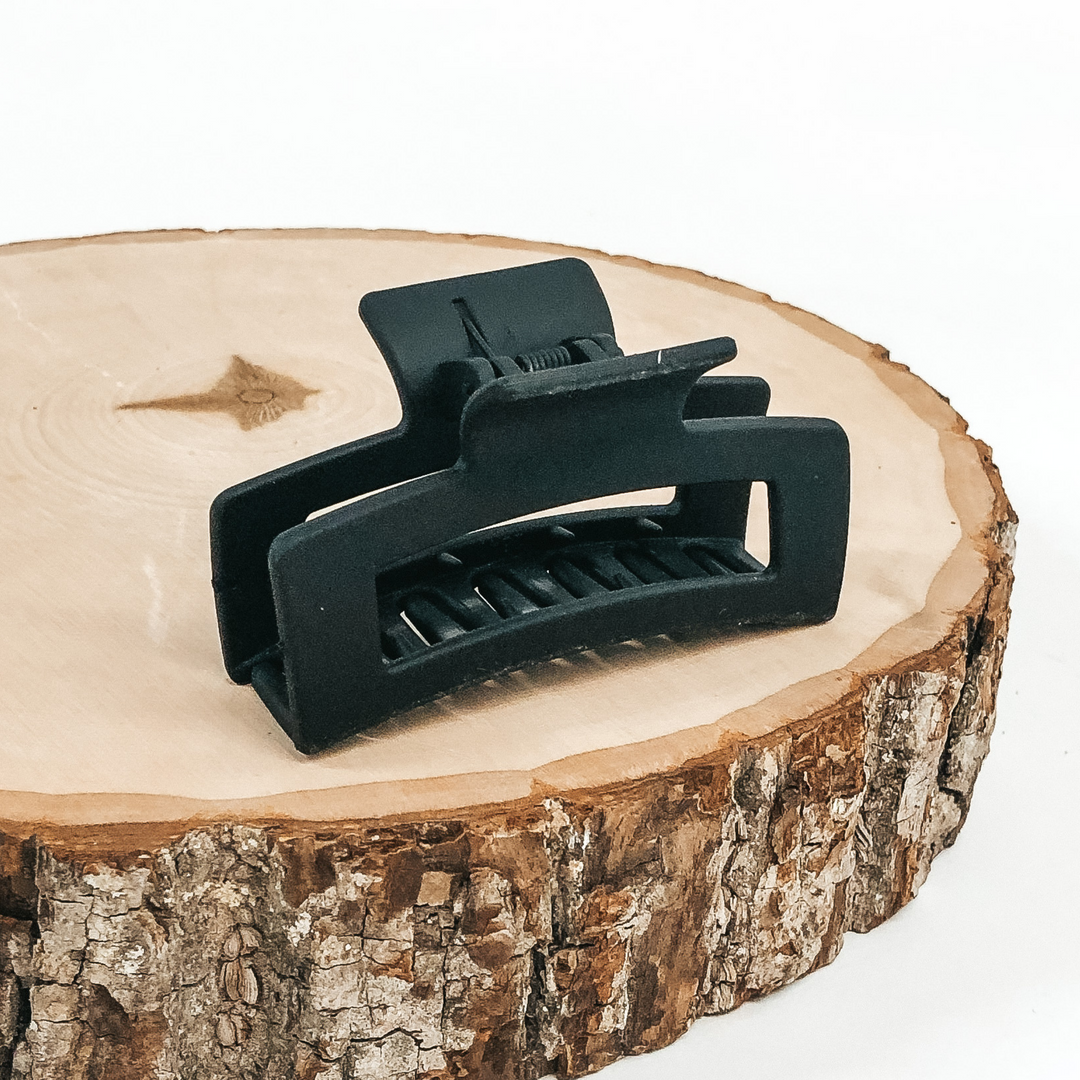 Matte black rectangle claw clip with rectangle cutout. This clip is pictured on a piece of wood on a white background.