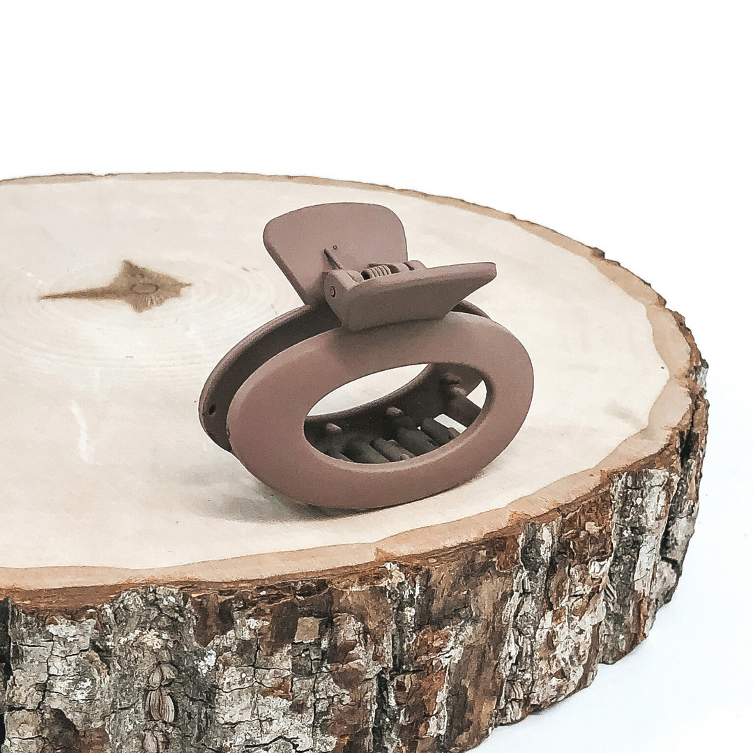 Matte taupe oval claw clip with an oval cutout. This clip is pictured on a piece of wood on a white background.