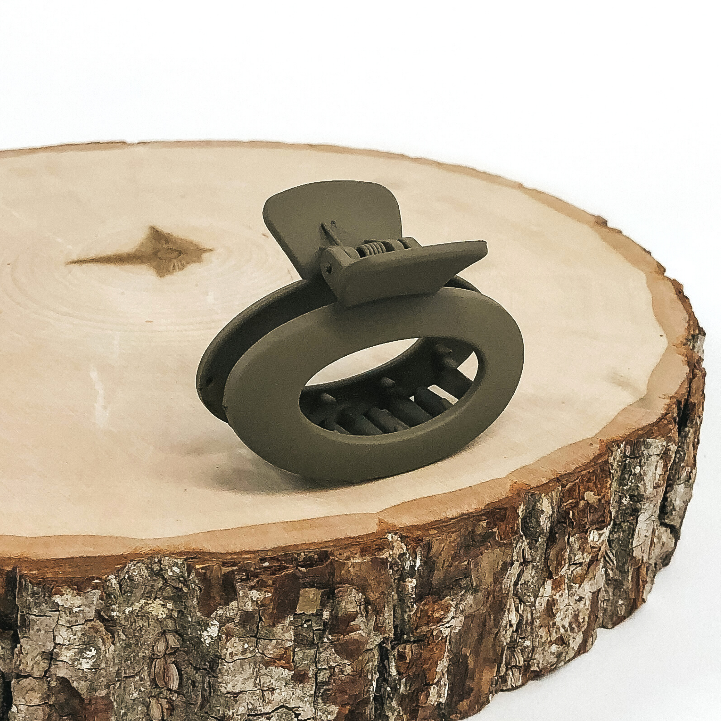 Matte olive green oval claw clip with an oval cutout. This clip is pictured on a piece of wood on a white background.