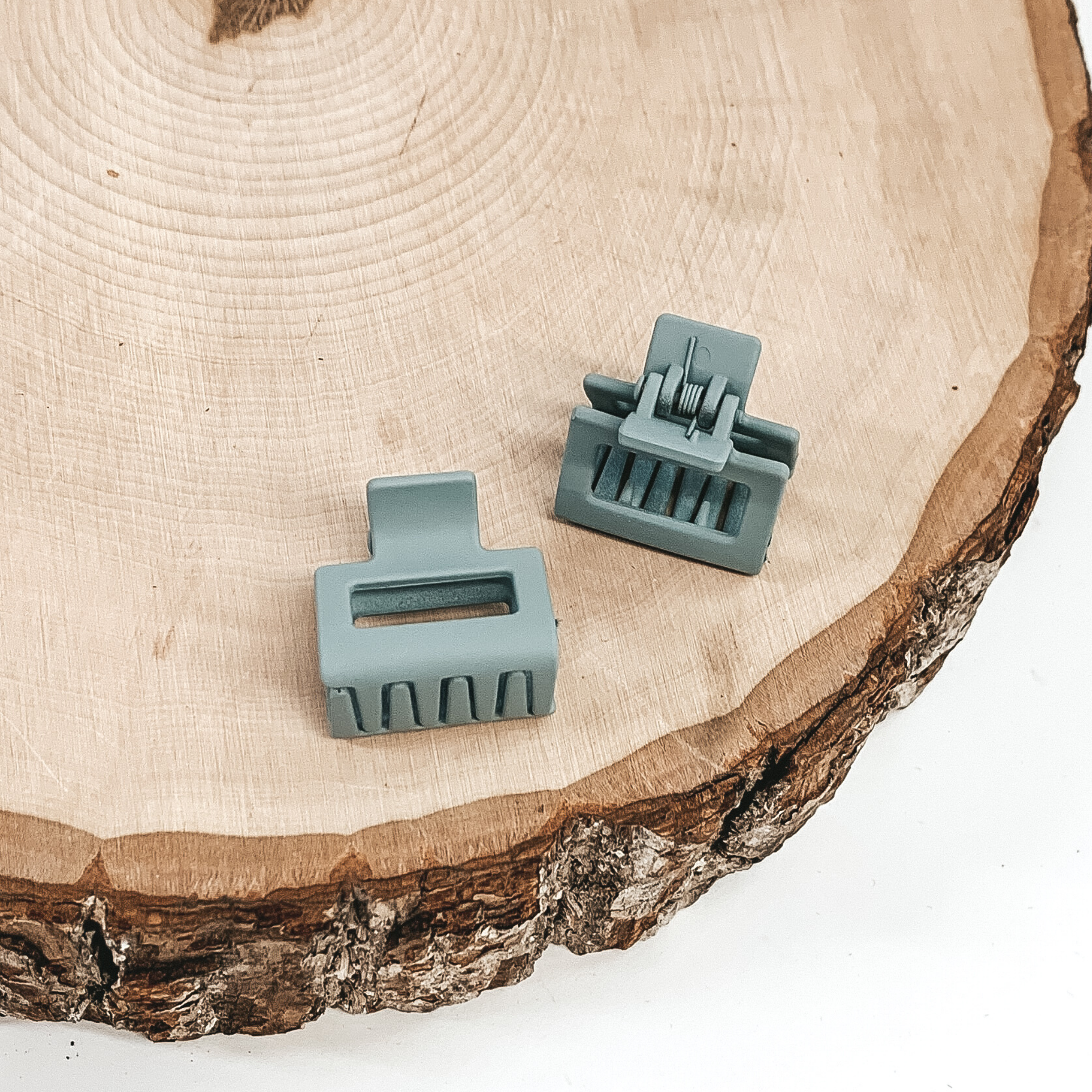 Matte dusty blue rectangle claw clips with a rectangle cutout. This clip is pictured on a piece of wood on a white background.