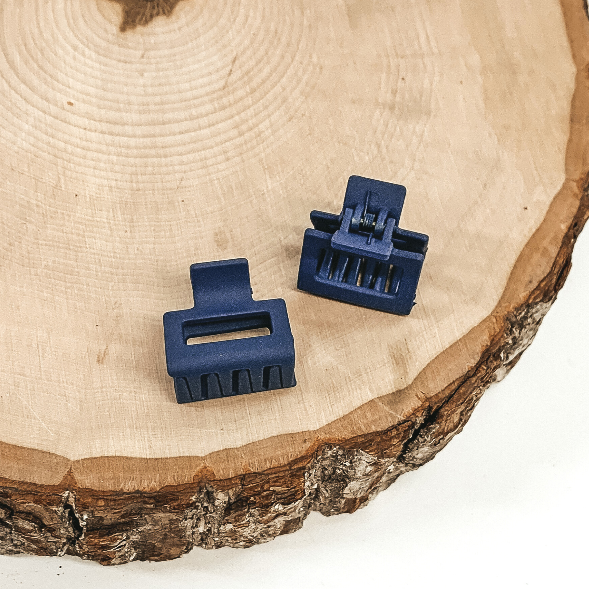 Matte navy blue rectangle claw clips with a rectangle cutout. This clip is pictured on a piece of wood on a white background.