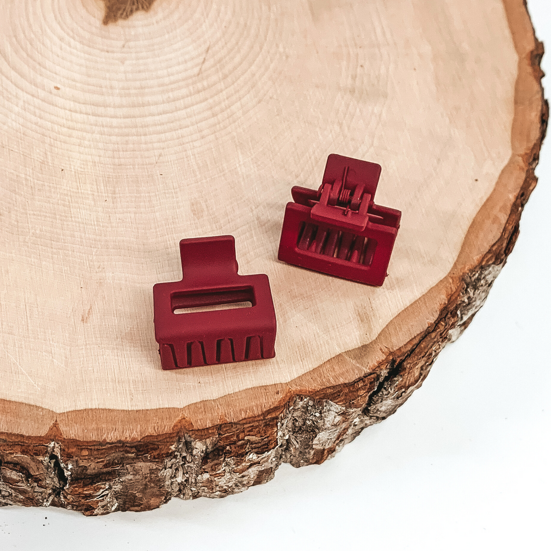 Matte red rectangle claw clips with a rectangle cutout. This clip is pictured on a piece of wood on a white background.