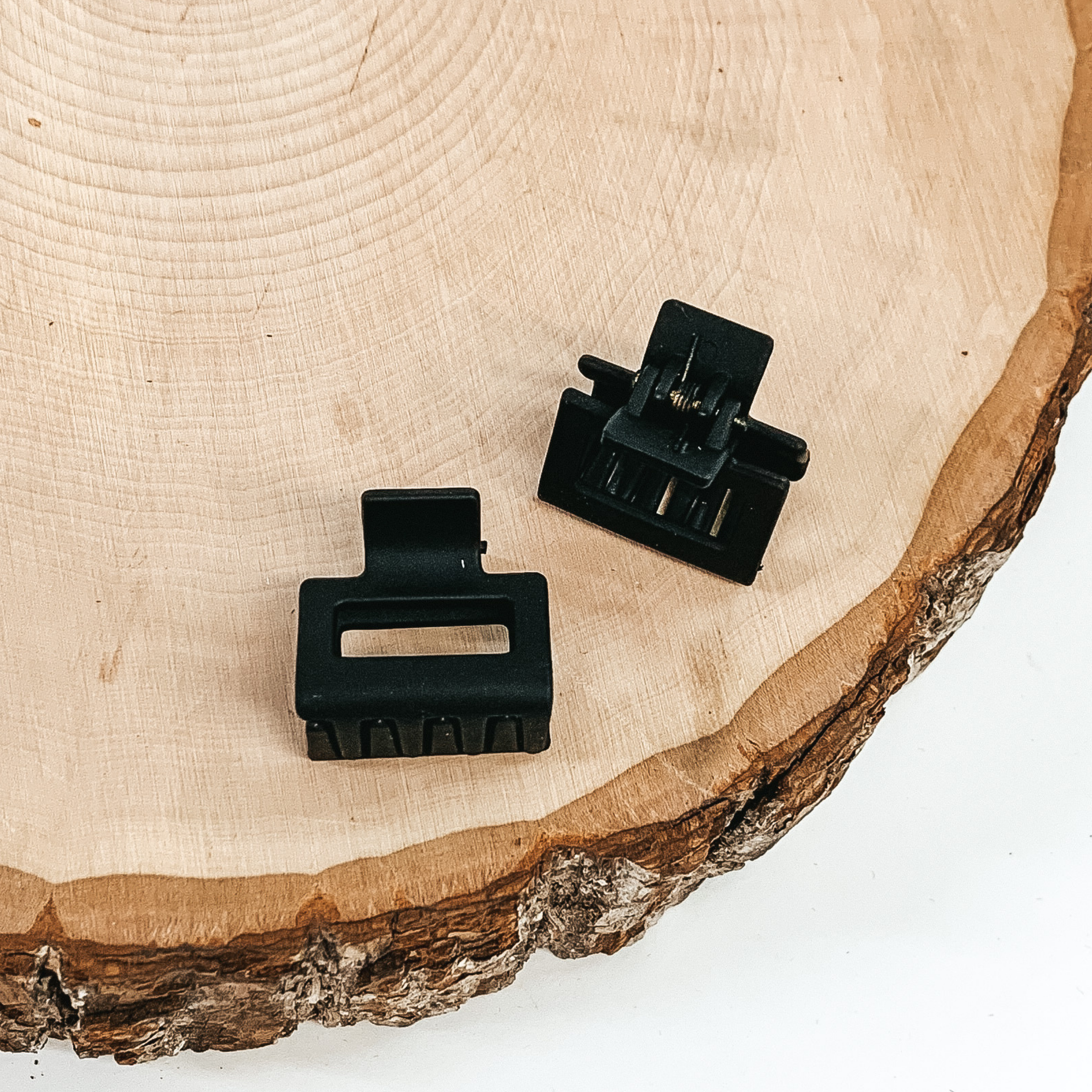 Matte black rectangle claw clips with a rectangle cutout. This clip is pictured on a piece of wood on a white background.
