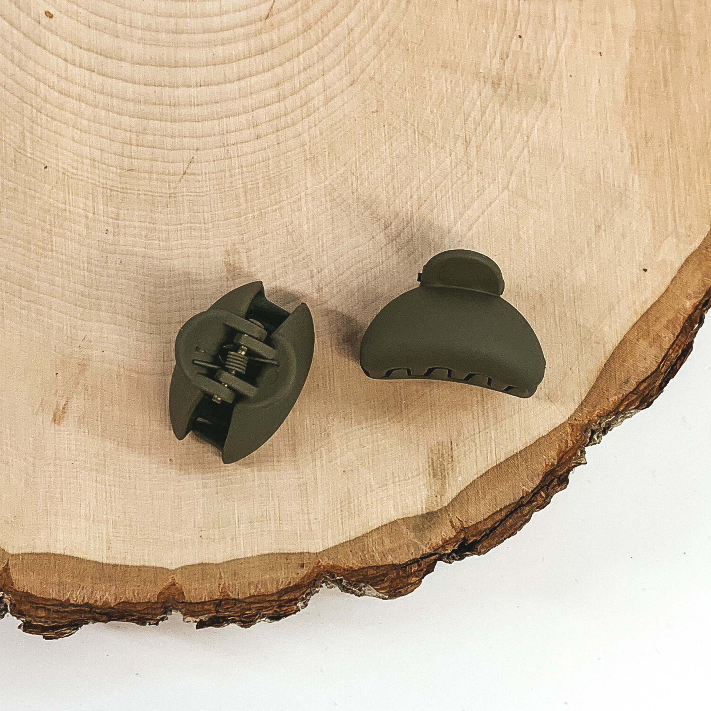 Matte olive green oval claw clips with an oval cutout. This clip is pictured on a piece of wood on a white background.