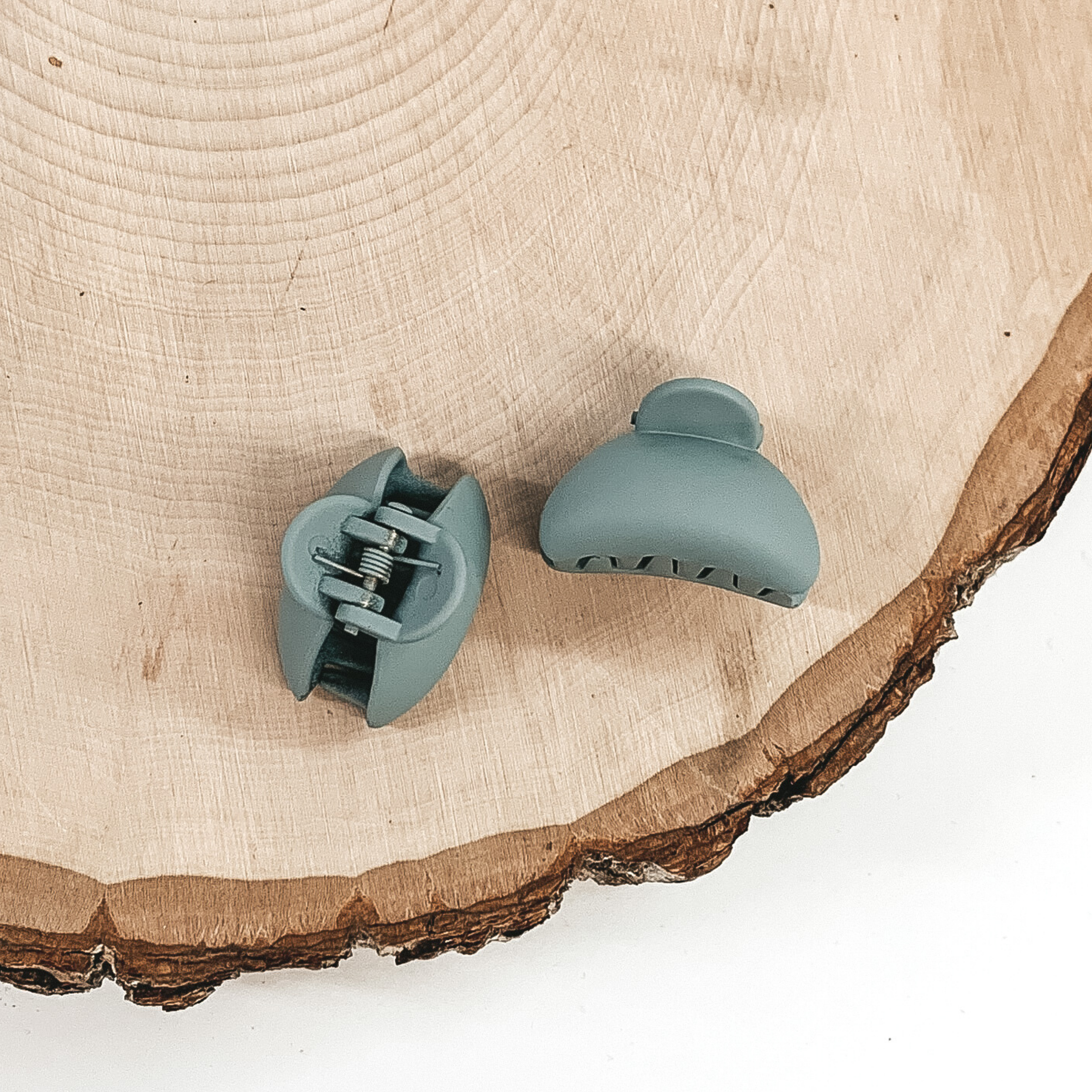 Matte dust blue oval claw clips with an oval cutout. This clip is pictured on a piece of wood on a white background.