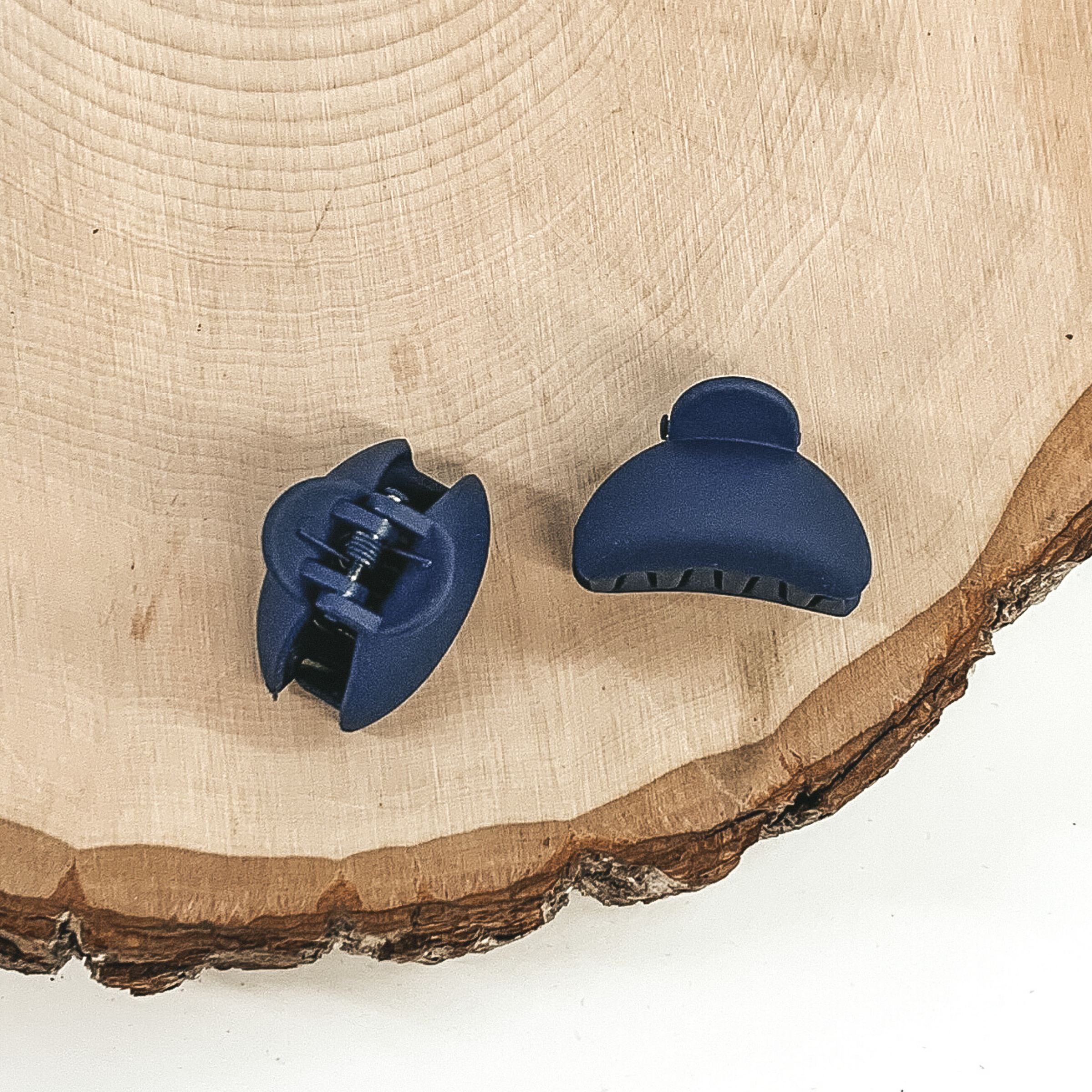 Matte navy blue oval claw clips with an oval cutout. This clip is pictured on a piece of wood on a white background.