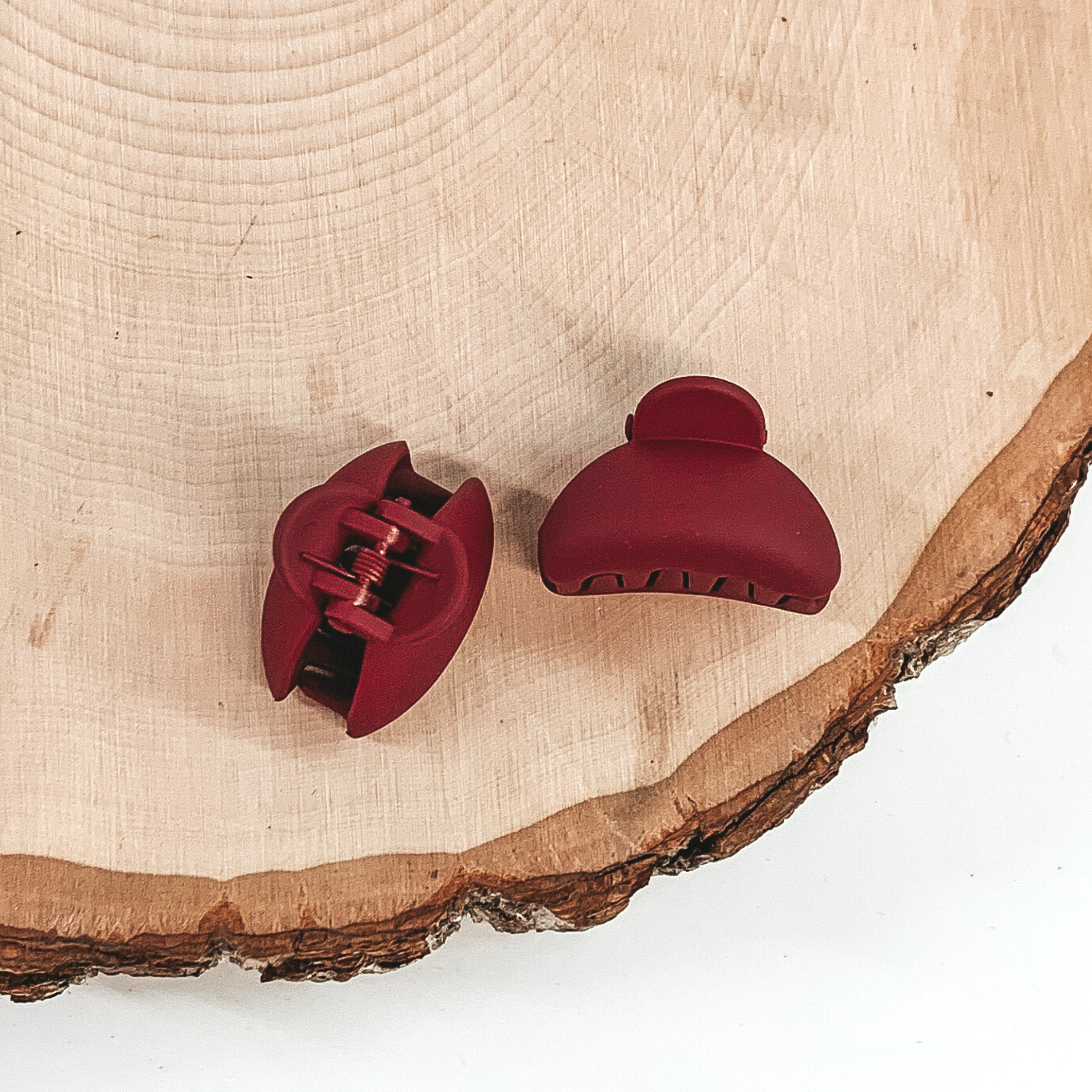 Matte red oval claw clips with an oval cutout. This clip is pictured on a piece of wood on a white background.