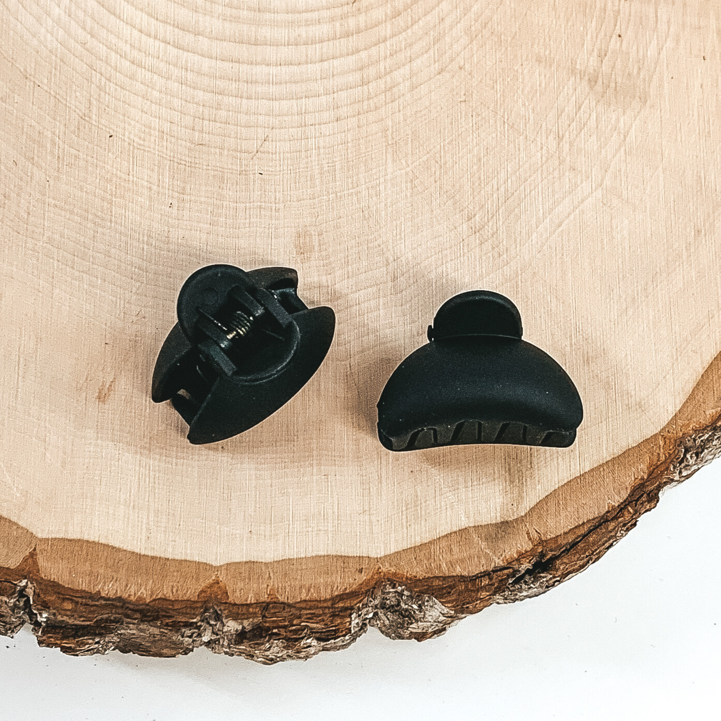 Matte black oval claw clips with an oval cutout. This clip is pictured on a piece of wood on a white background.