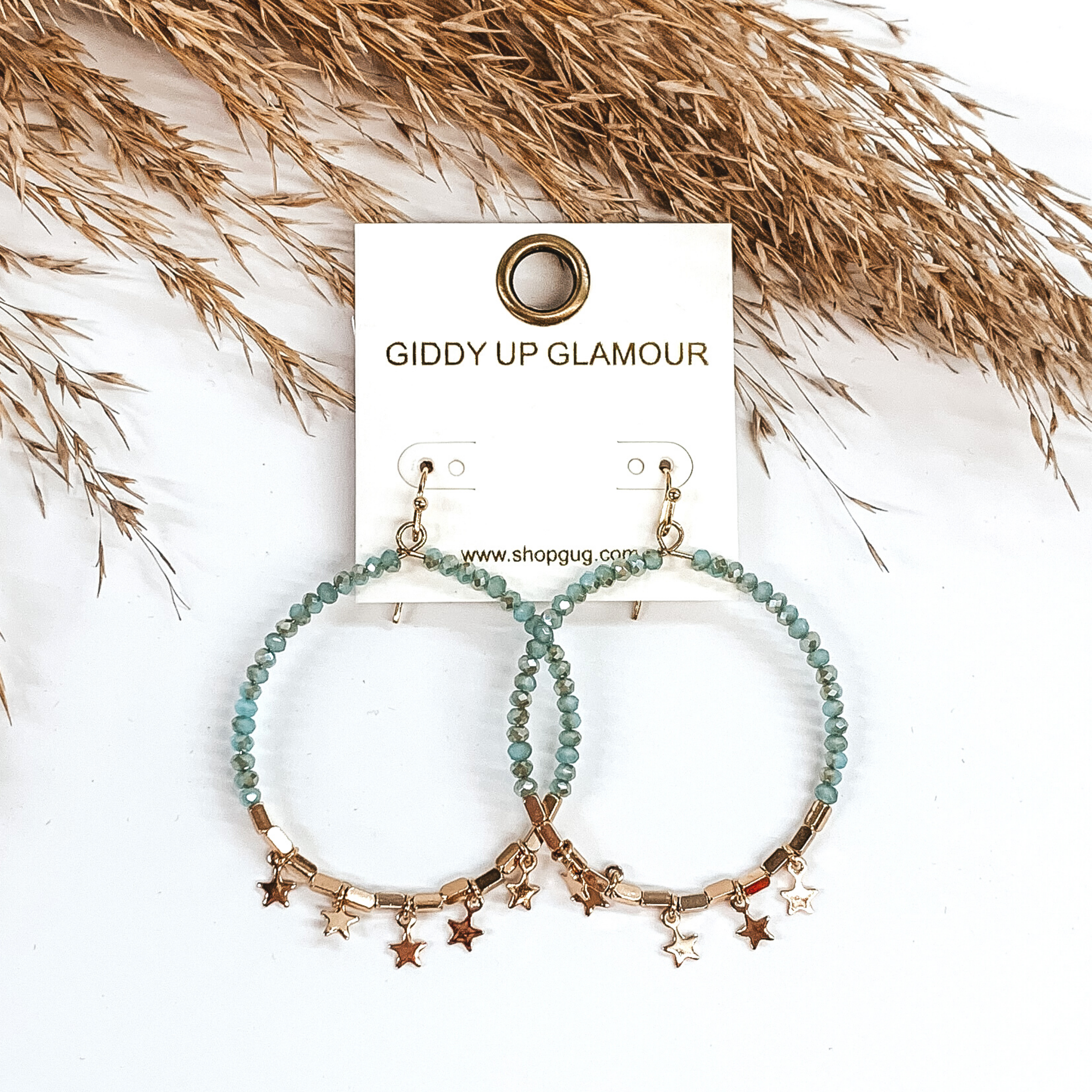 These earrings are a circle drop earrings covered half in turquoise beads and the bottom part has gold beads with tiny gold star charms. These earrings are pictured on a white background with tan floral at the top of the picture. 