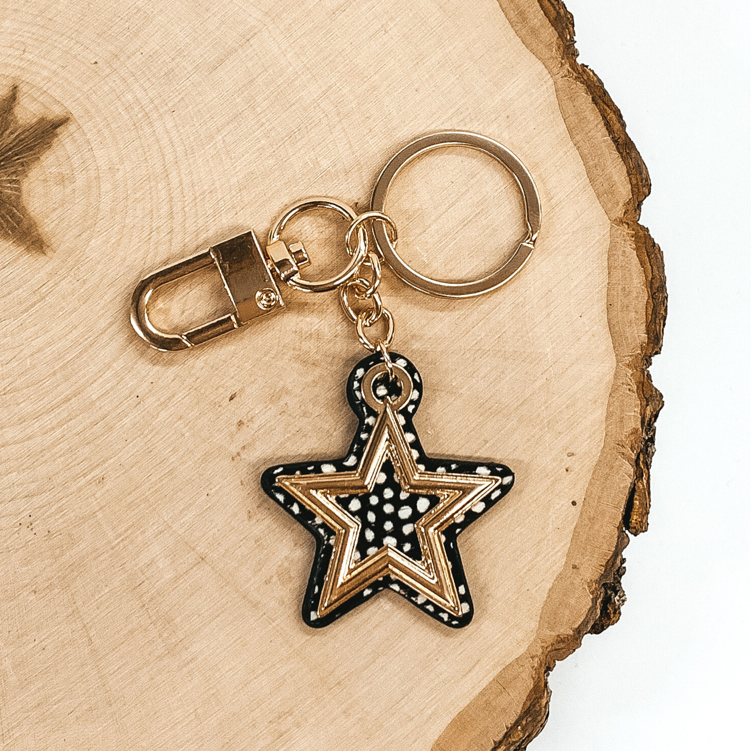 Gold key chain with a black hide inlay with white dotted print star pendant that includes a gold star outline. This key chain is pictured on a piece of wood on a white background.