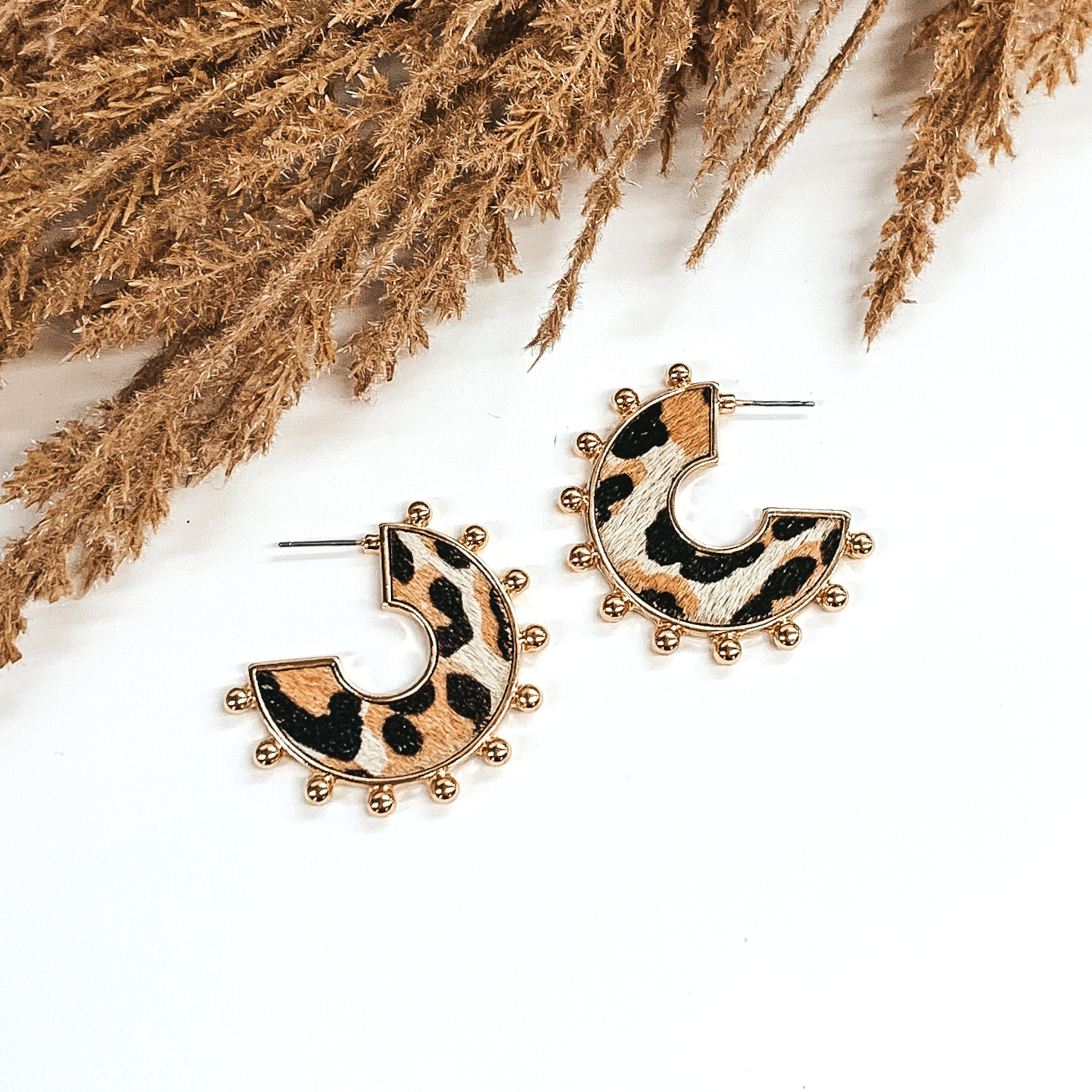 Flat hoops with white animal hide inlay with black and brown animal print pattern. These hoops have gold beads on the edge of the earrings. These earrings are pictured o  white background with tan floral at the top of the page.