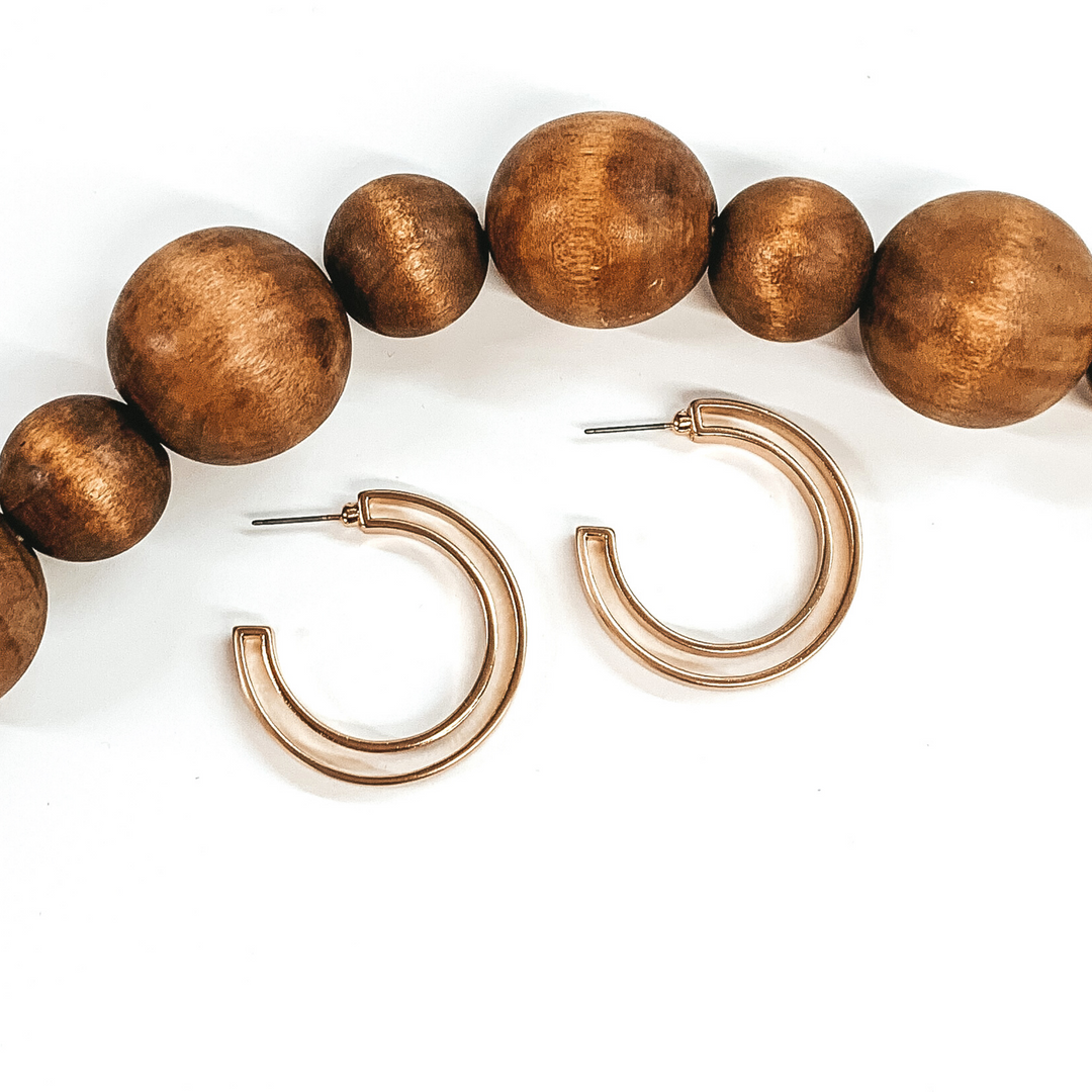 Laying on a white background are two gold hoop earrings. They are a circle double layered hoop earrings. There are brown decor beads above the earrings. 