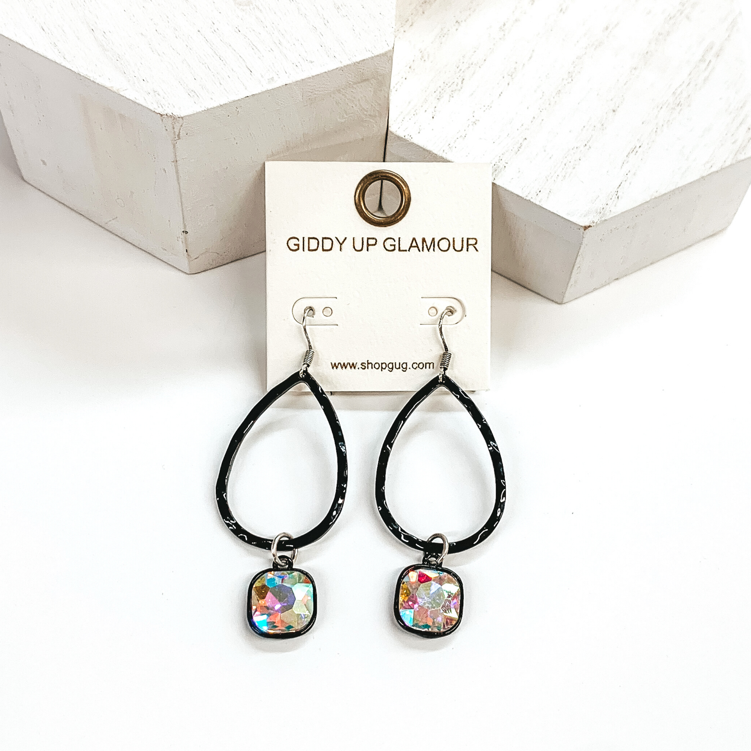 Black teardrop hammered earrings with a hanging cushion cut ab crystal. These earrings are pictured on a white background with white blocks at the top of the picture. 