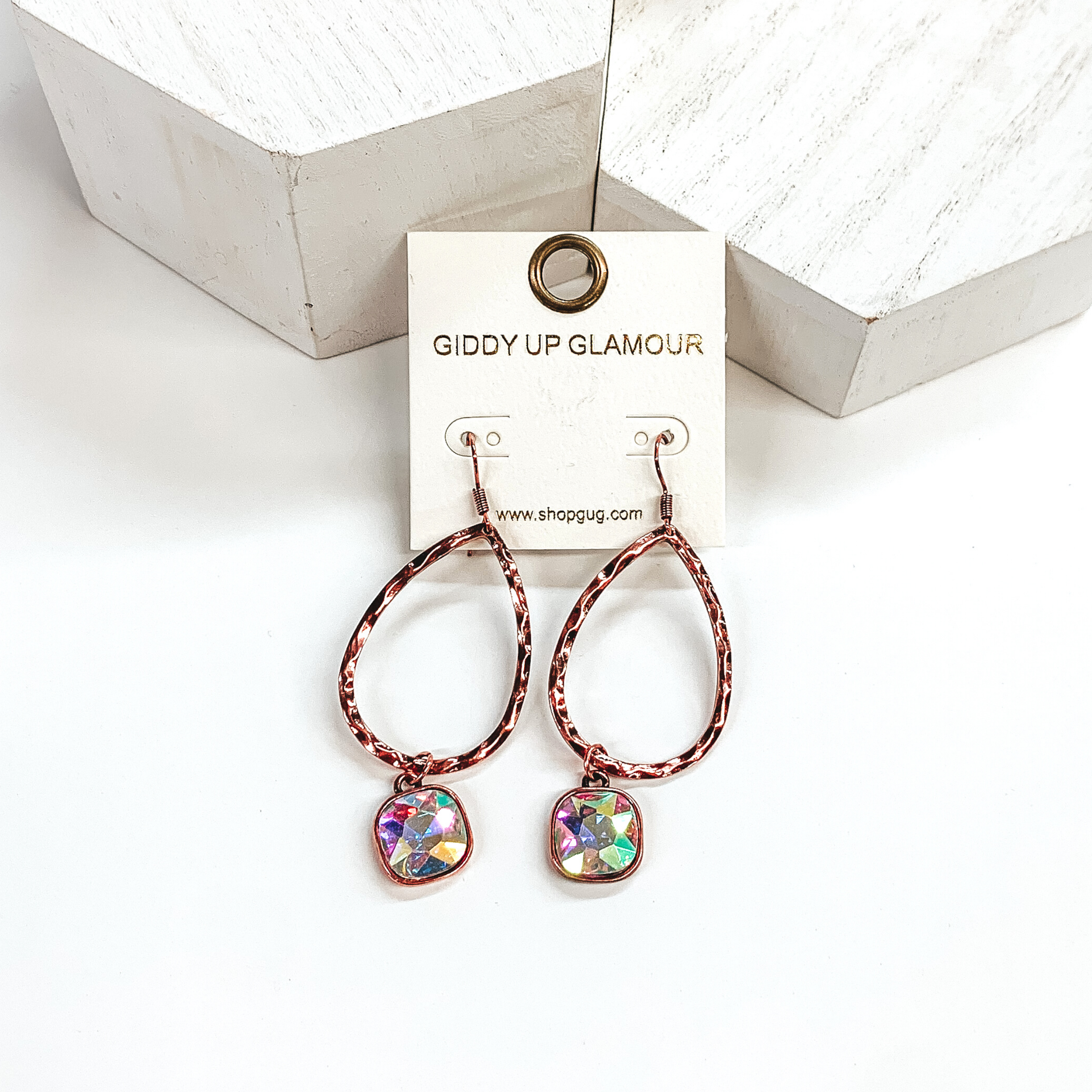 Copper teardrop hammered earrings with a hanging cushion cut ab crystal. These earrings are pictured on a white background with white blocks at the top of the picture. 