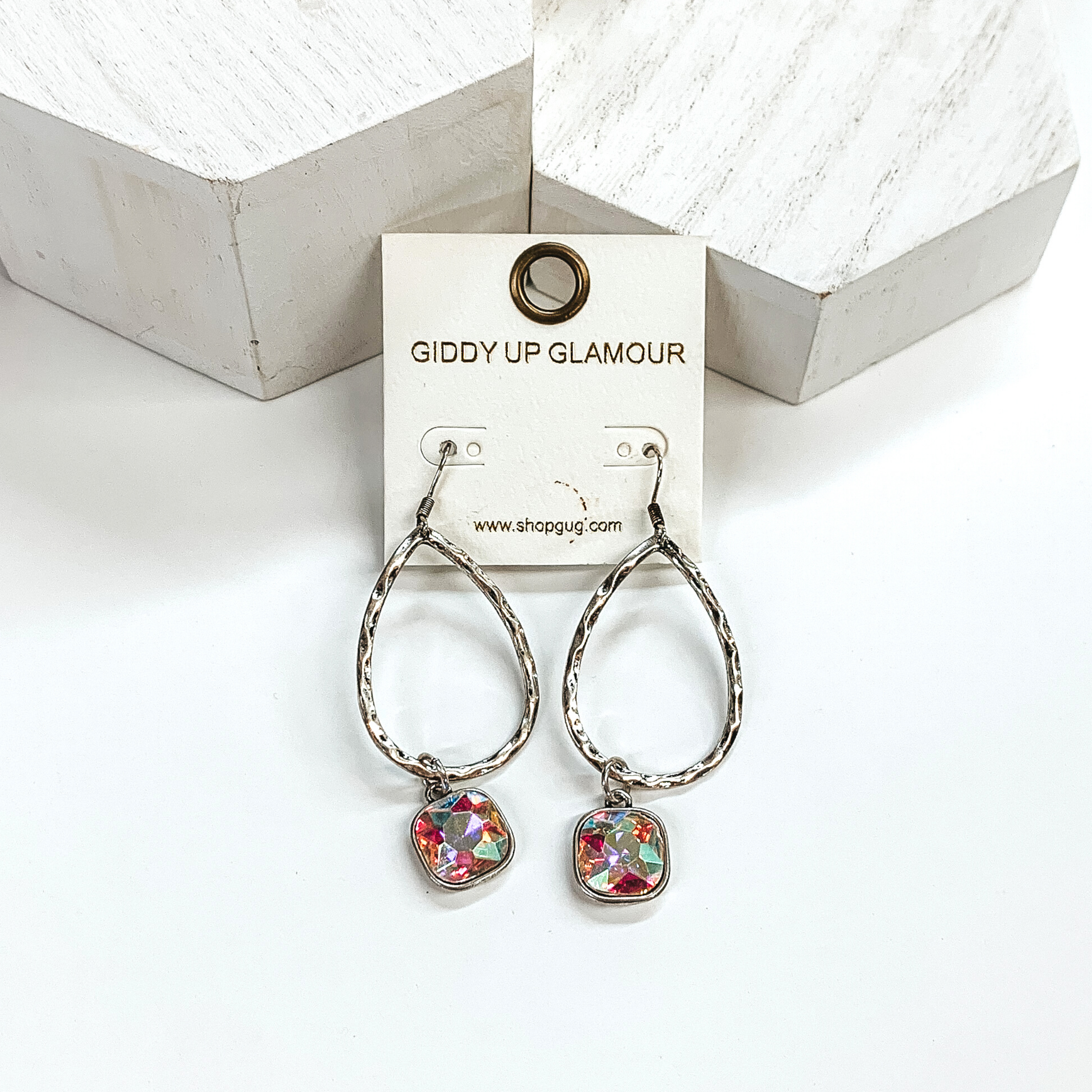 Silver teardrop hammered earrings with a hanging cushion cut ab crystal. These earrings are pictured on a white background with white blocks at the top of the picture. 