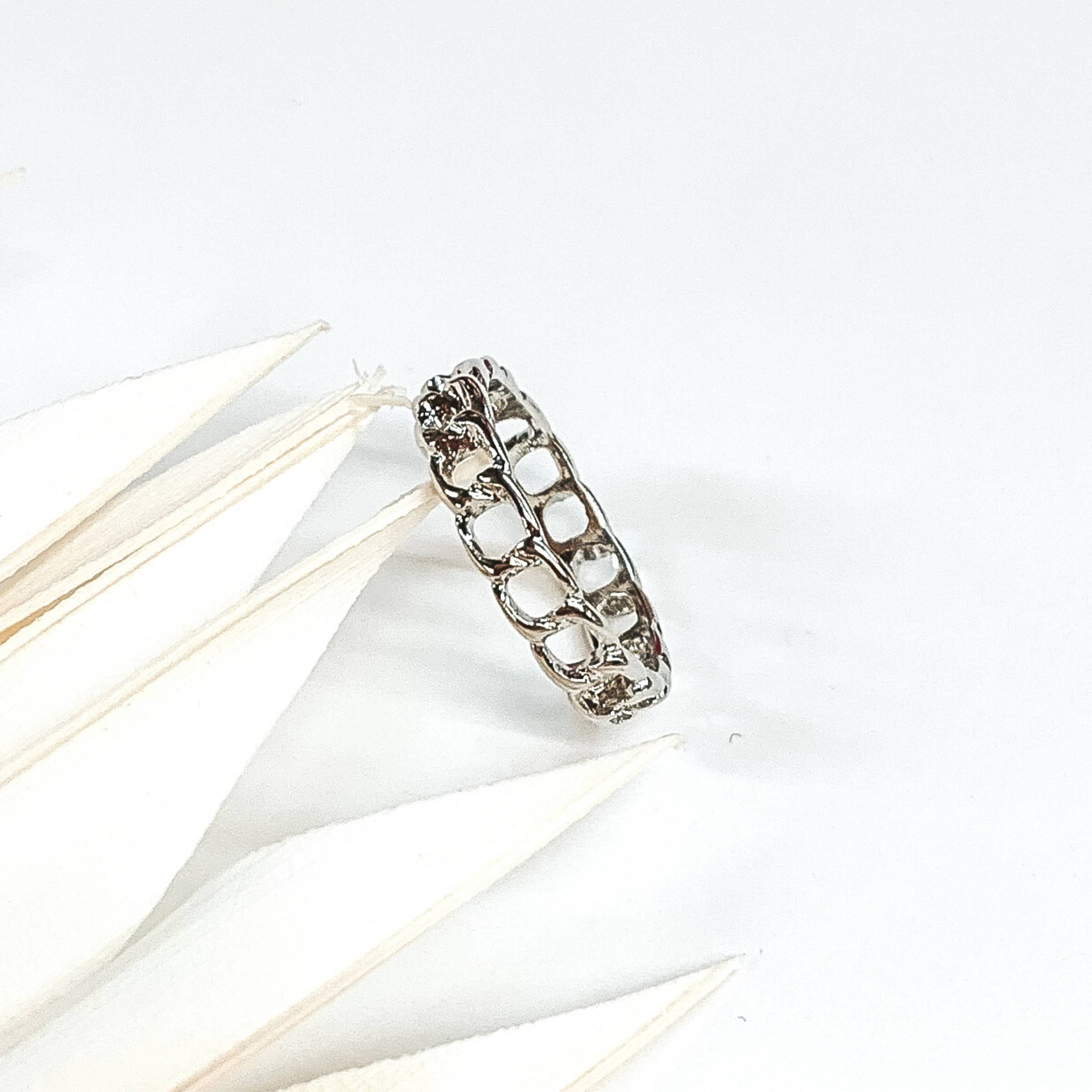 This is a silver chain link ring. this ring is on a white background with some white leaves on the left side of the picture. 