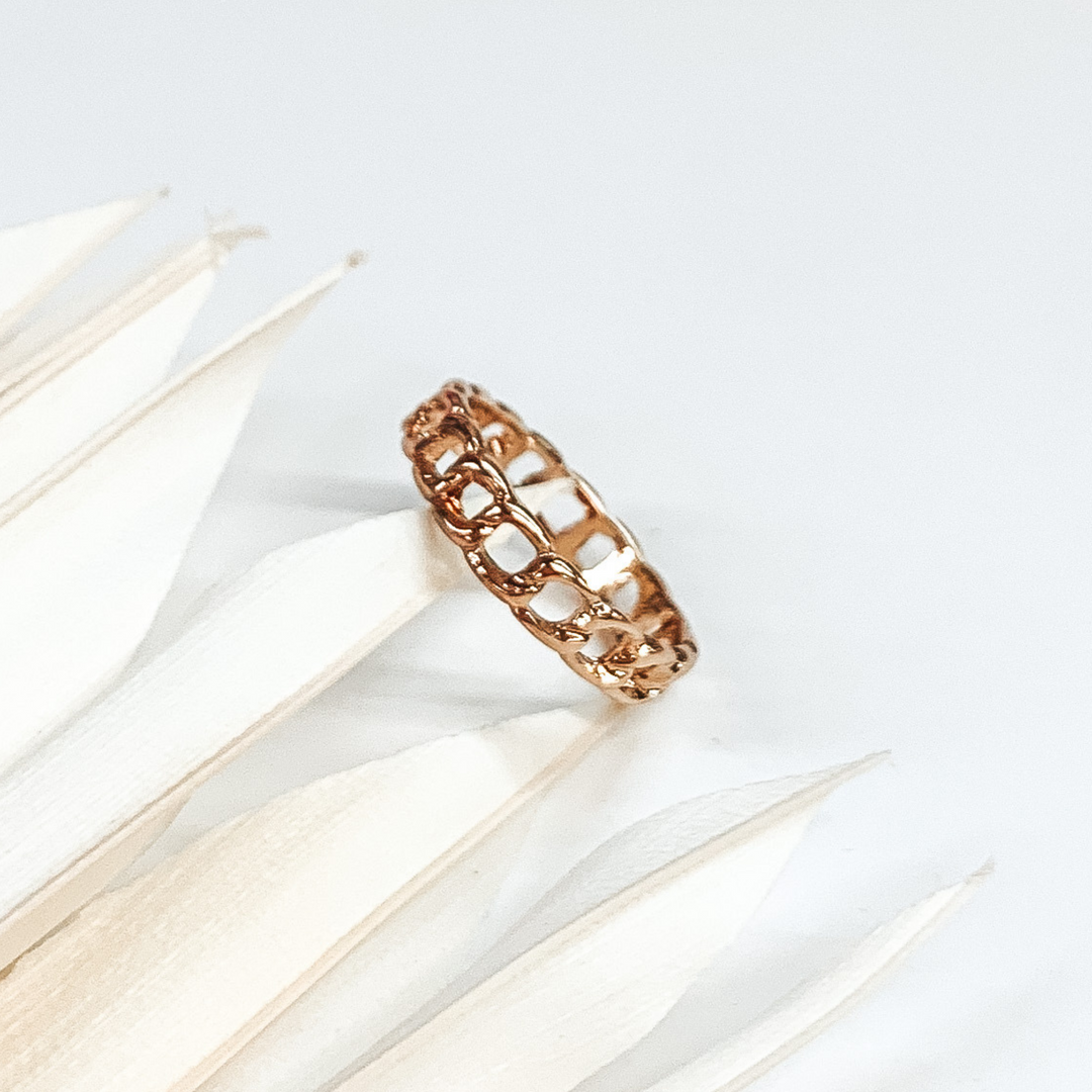 This is a gold chain link ring. this ring is on a white background with some white leaves on the left side of the picture.