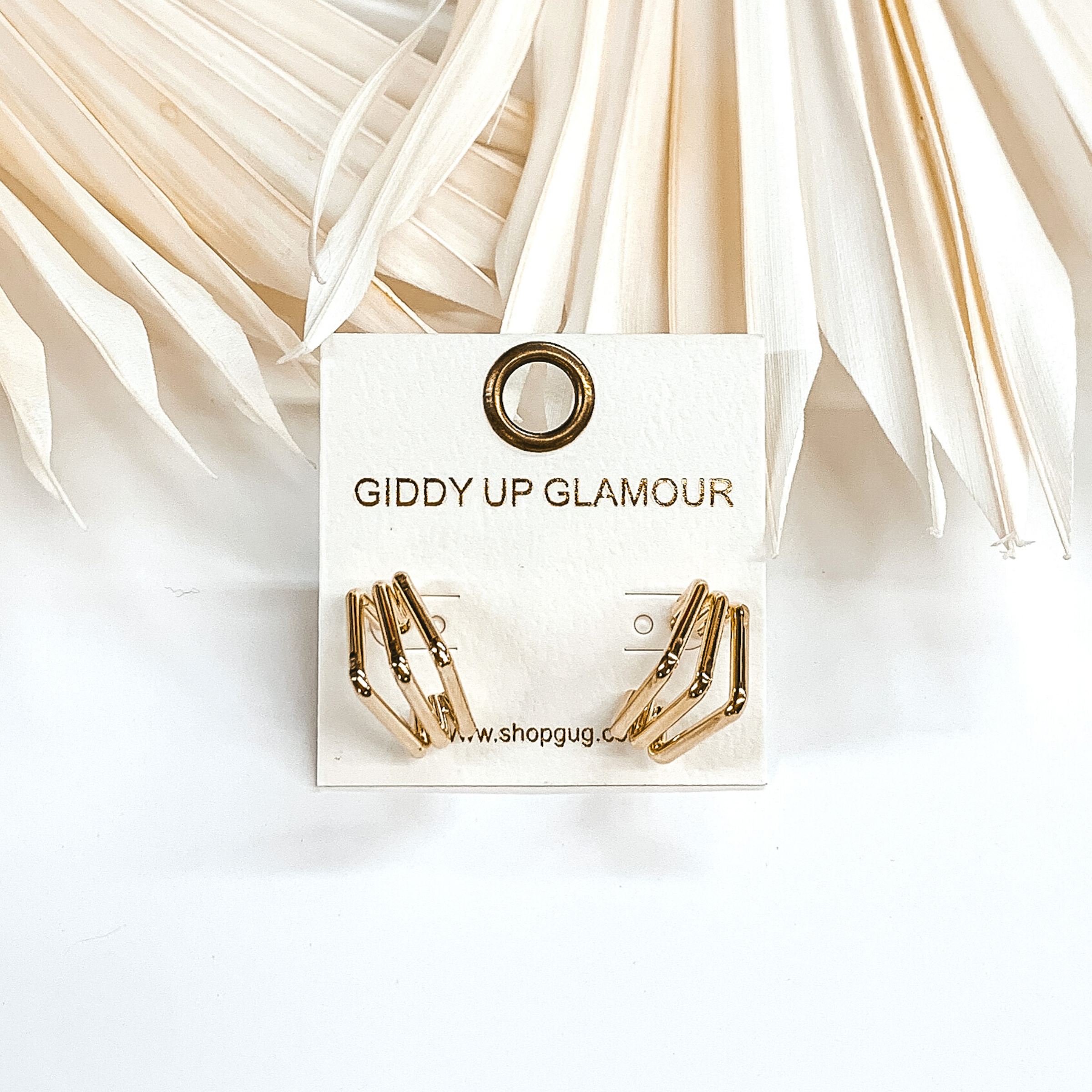 Gold triple, square hoops that are pictured on an earrings holder that is sitting on a white background.