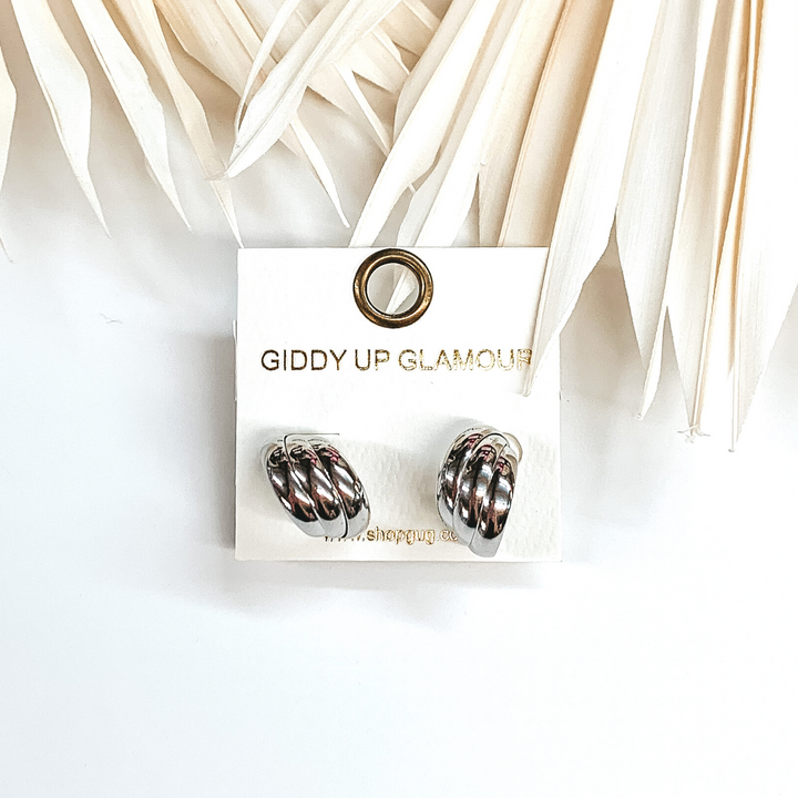 Silver triple layered circle hoops that are pictured on an earrings holder that is sitting on a white background with ivory leaves. 