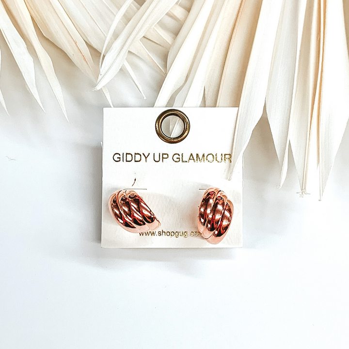 Rose gold triple layered circle hoops that are pictured on an earrings holder that is sitting on a white background with ivory leaves. 