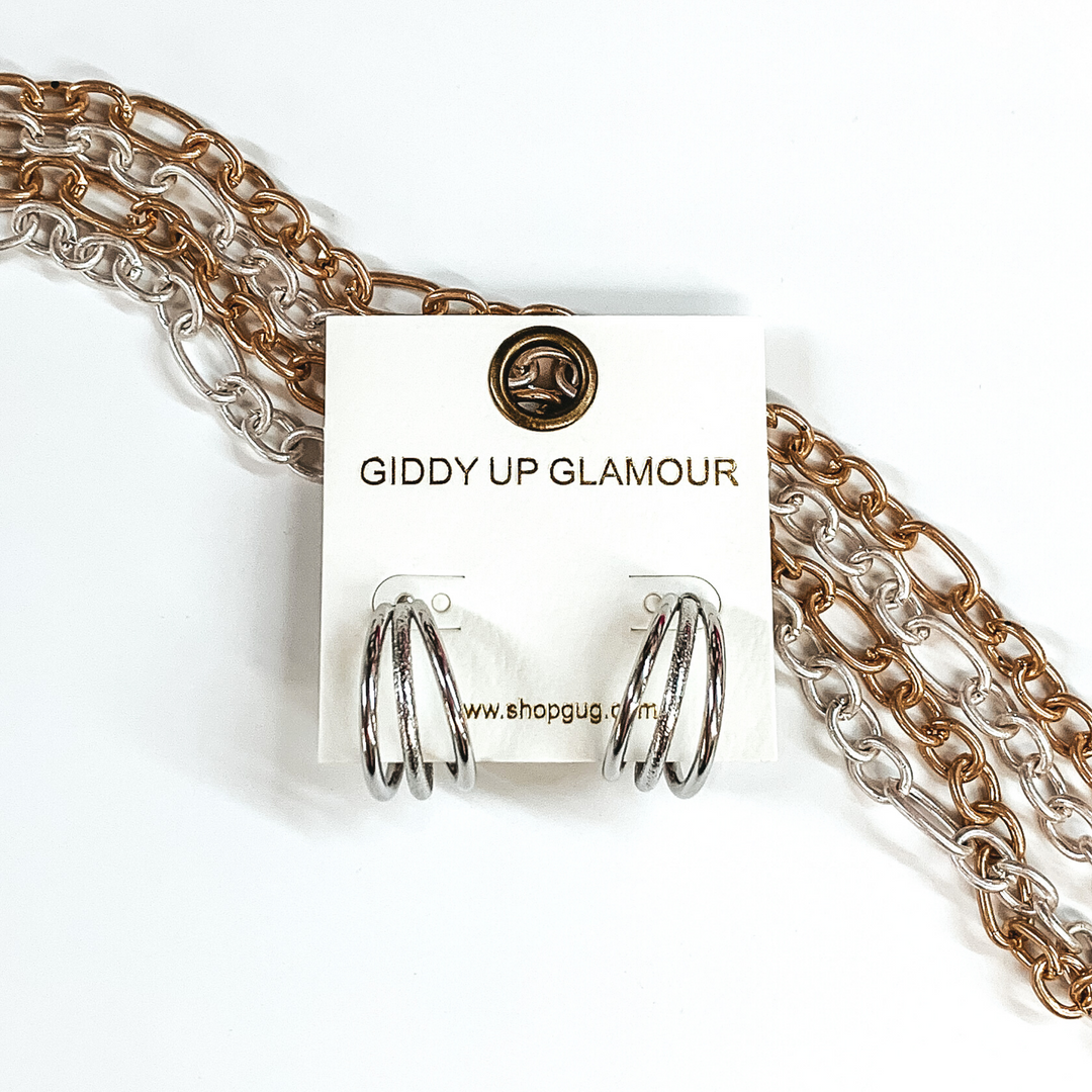 Silver triple circle hoop earrings. These earrings are pictured on an earring back laying on some gold and silver chains on a white background. 