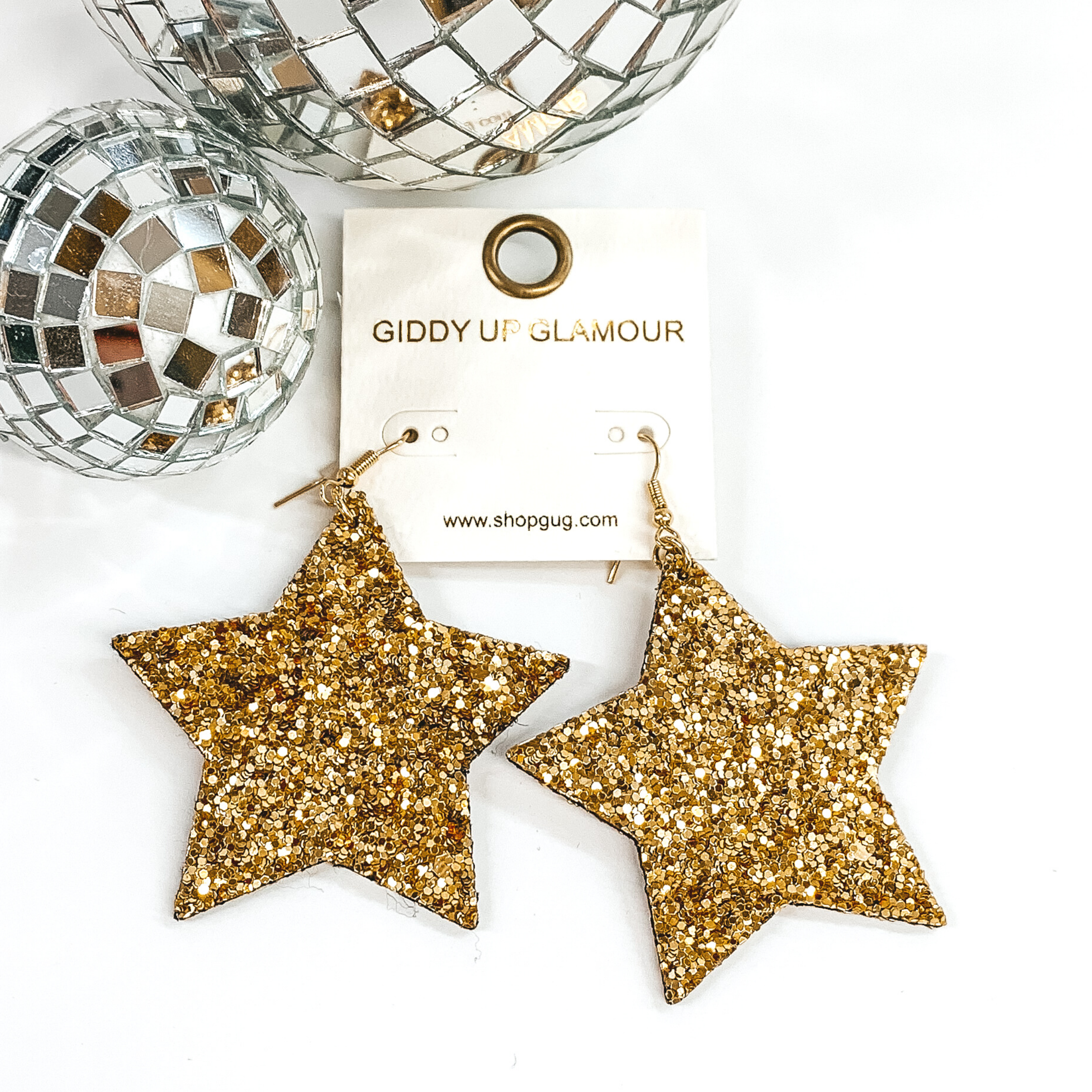 Glitter star dangle earrings in gold with a gold earrings hook. These earrings are pictured on a white background with a disco ball at the top of the picture.
